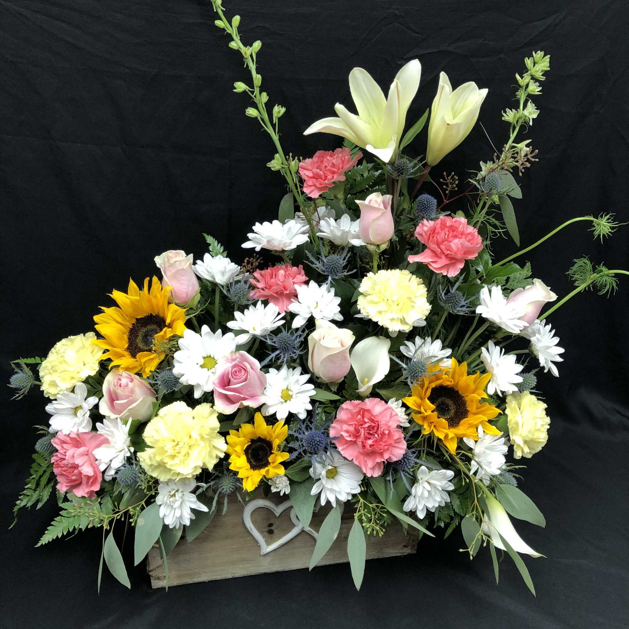 Mixed floral arrangement in a wooden box with lilies, roses, sunflowers, and daisies