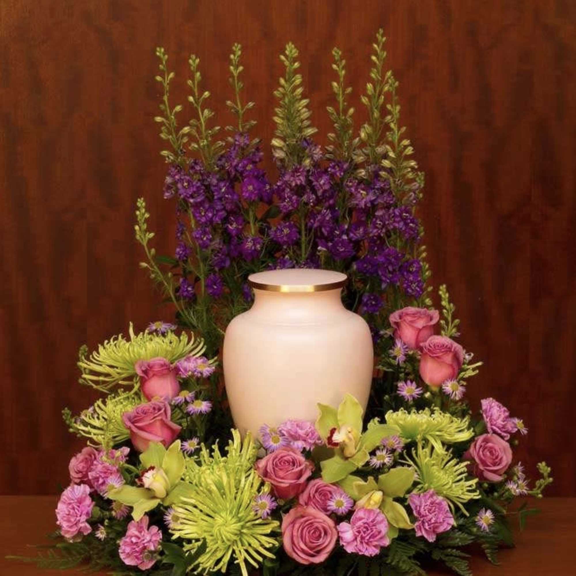 Pink roses and green spider mums arranged around a cream urn with purple flowers behind.