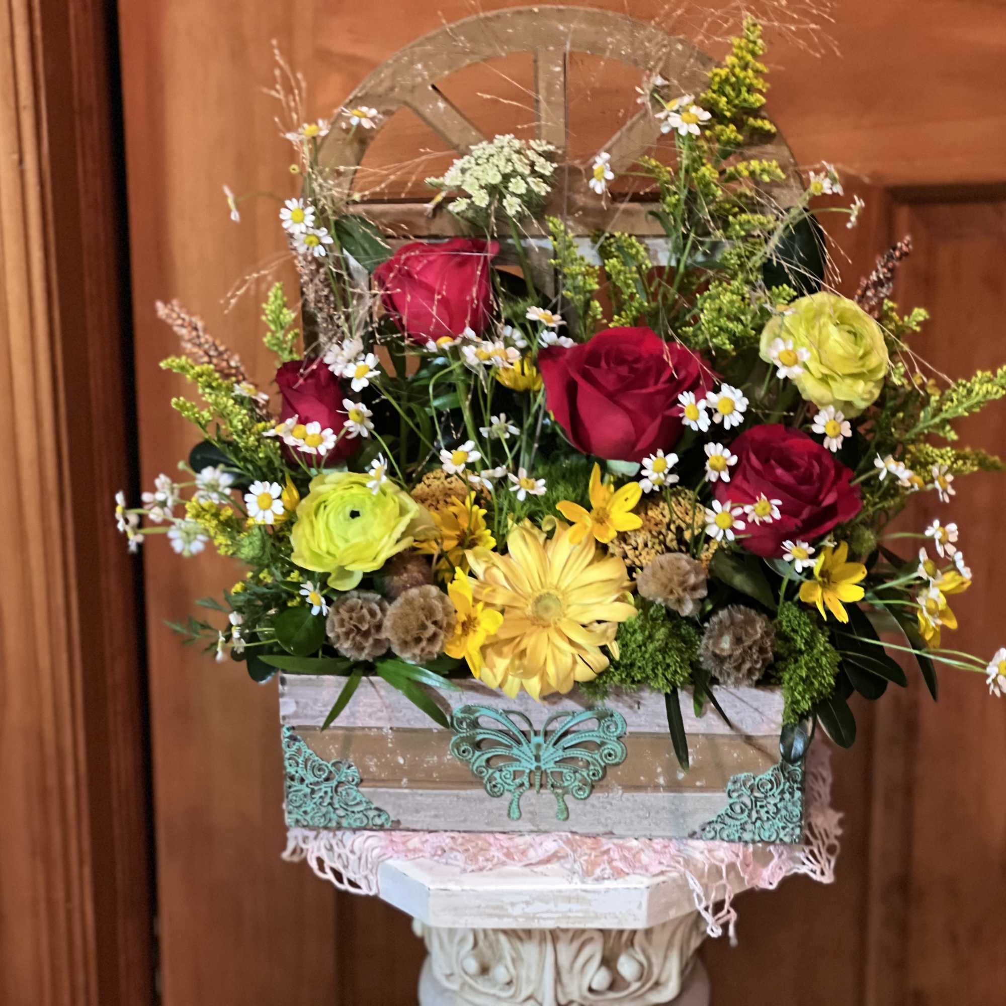 Mixed bouquet of red roses, yellow blooms, and small white daisies in a decorative box