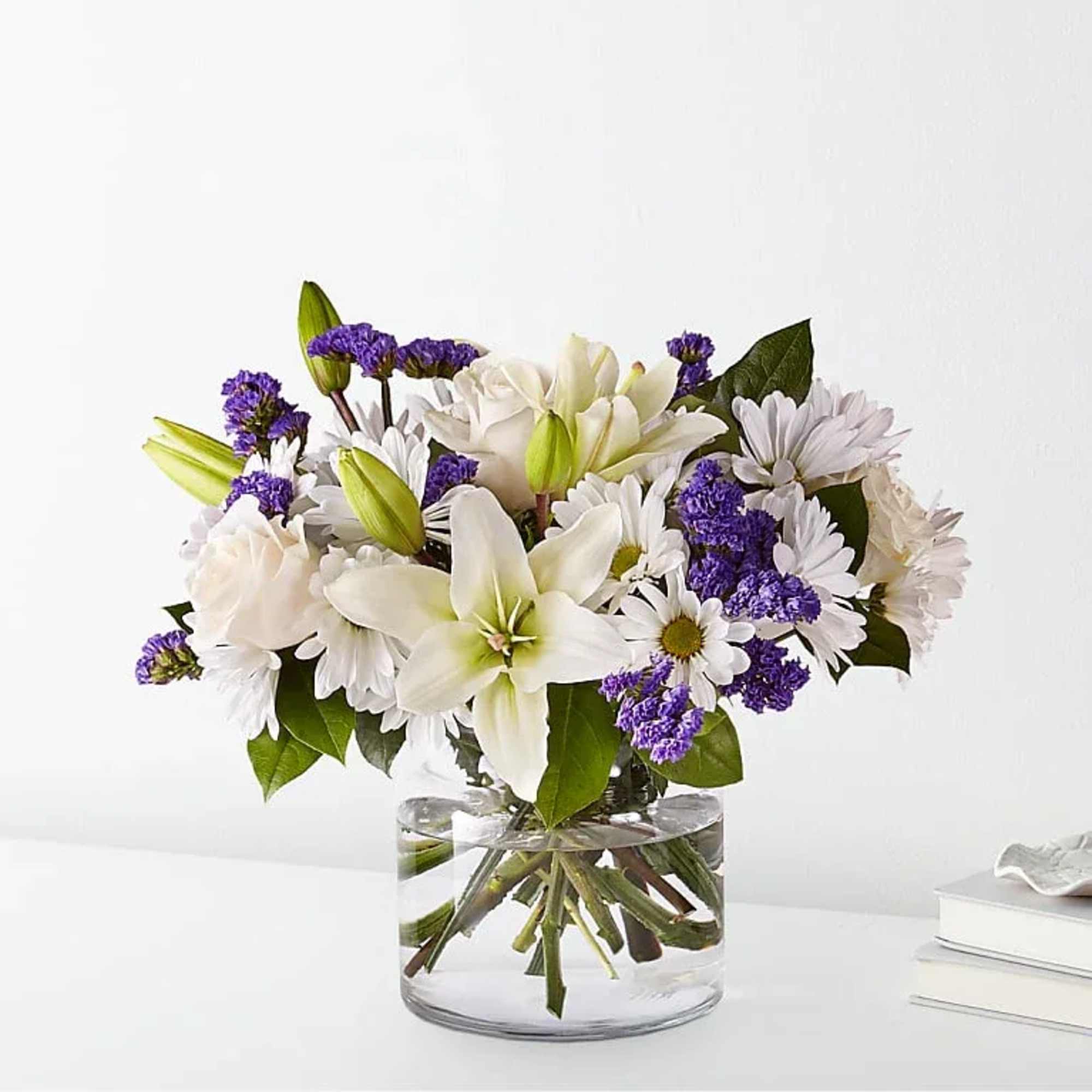 White lilies and daisies with purple filler in a clear glass vase