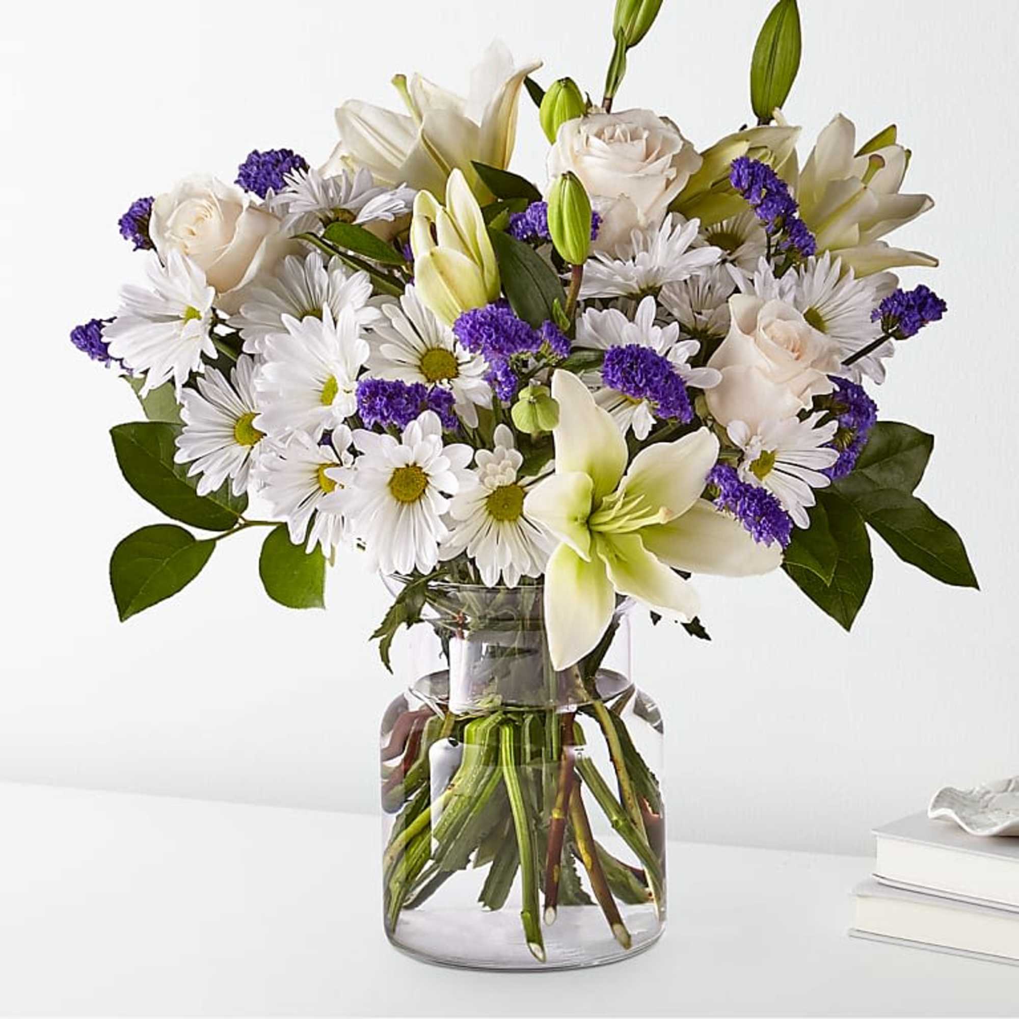White lilies, daisies, and roses arranged in a clear glass vase