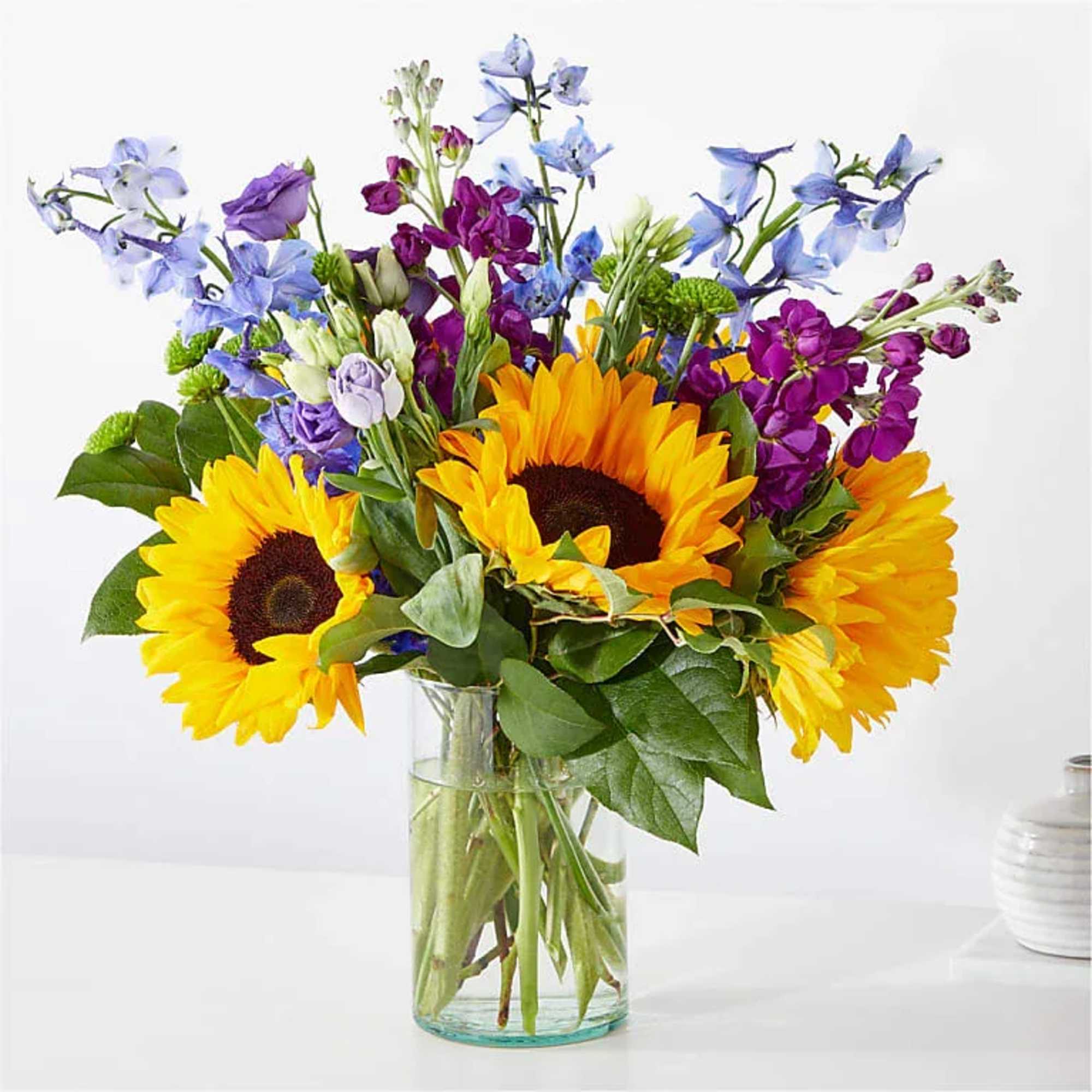 Bouquet of sunflowers, purple blooms, and blue flowers in a glass vase