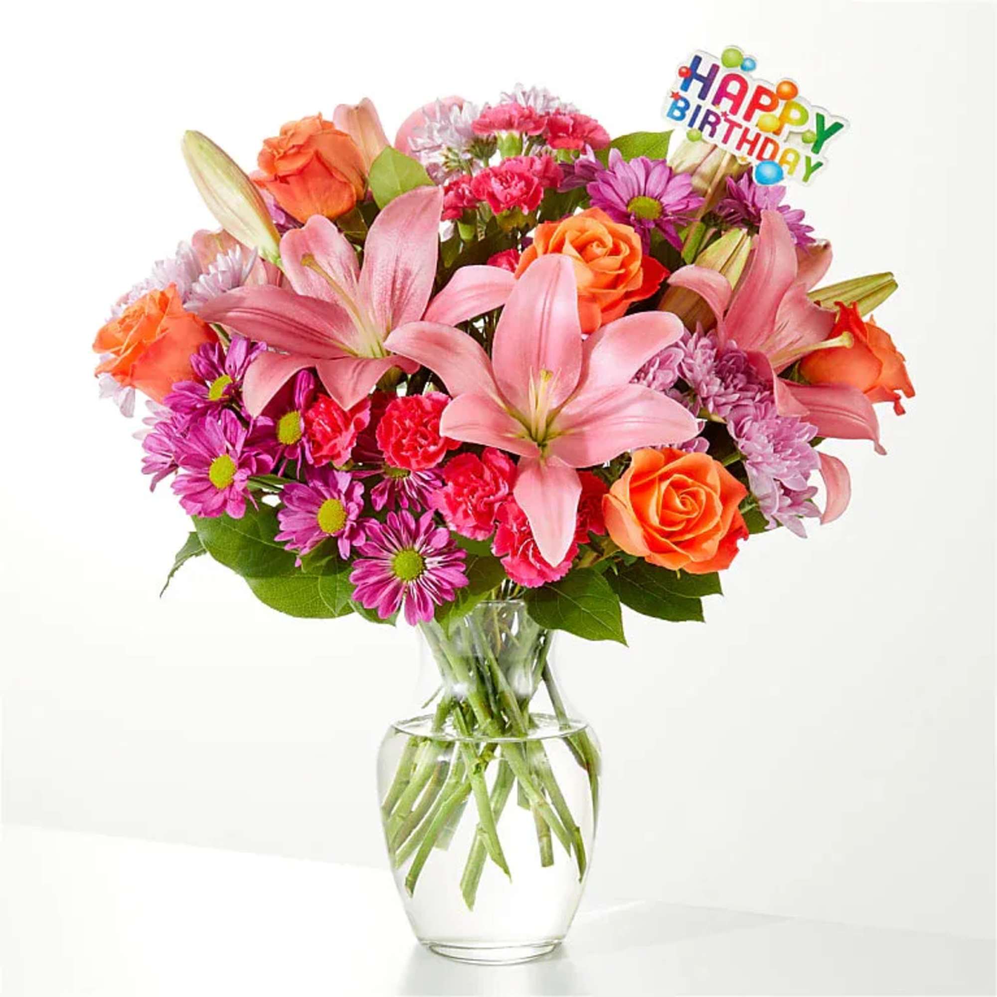Mixed bouquet of pink lilies, orange roses, and purple daisies in a glass vase