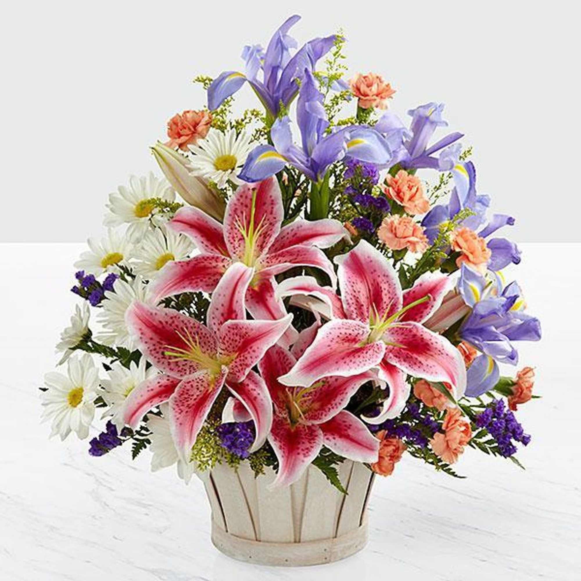 Mixed bouquet of pink lilies, purple irises, and white daisies in a basket