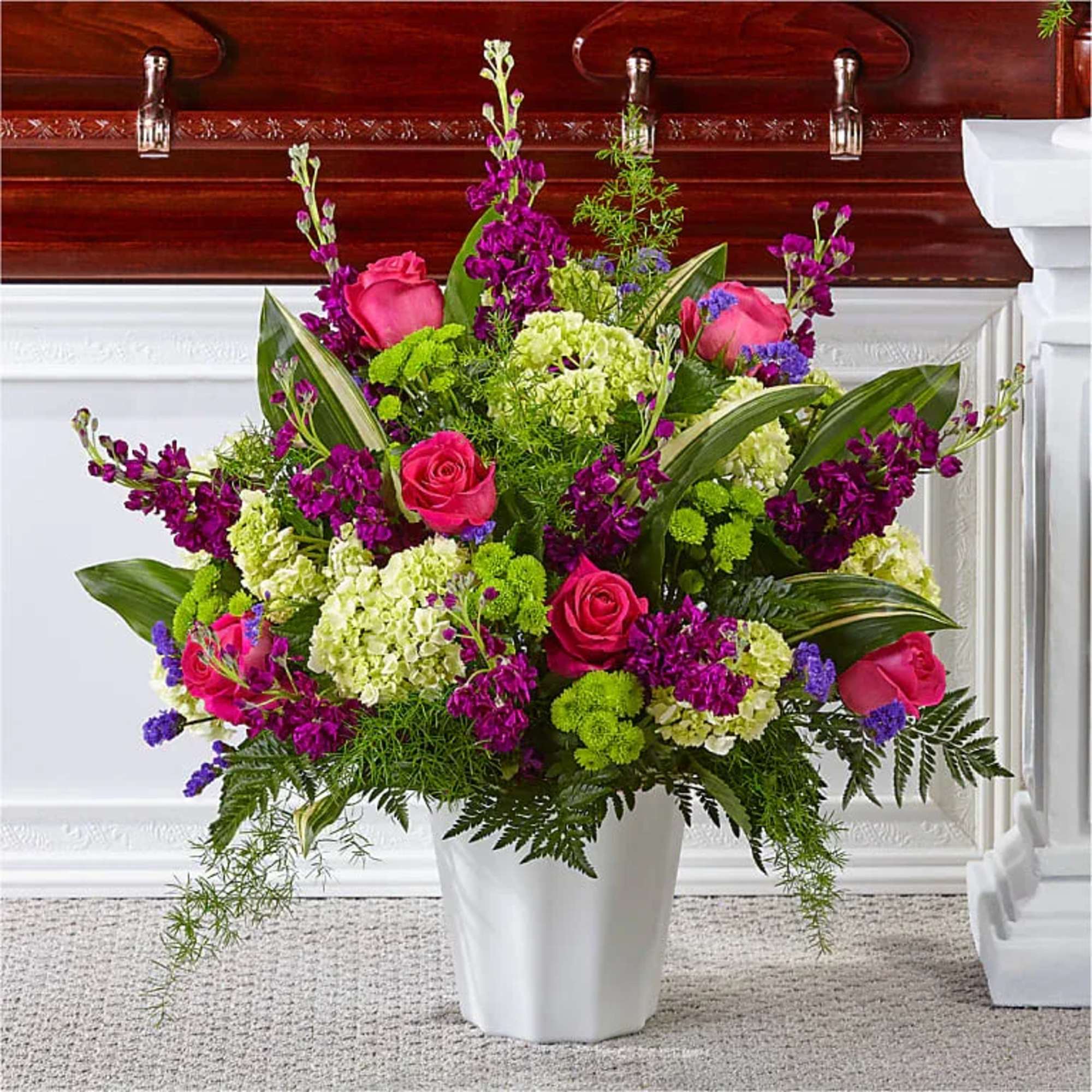 Tall arrangement of hot pink roses, purple blooms, and green hydrangeas in a white vase