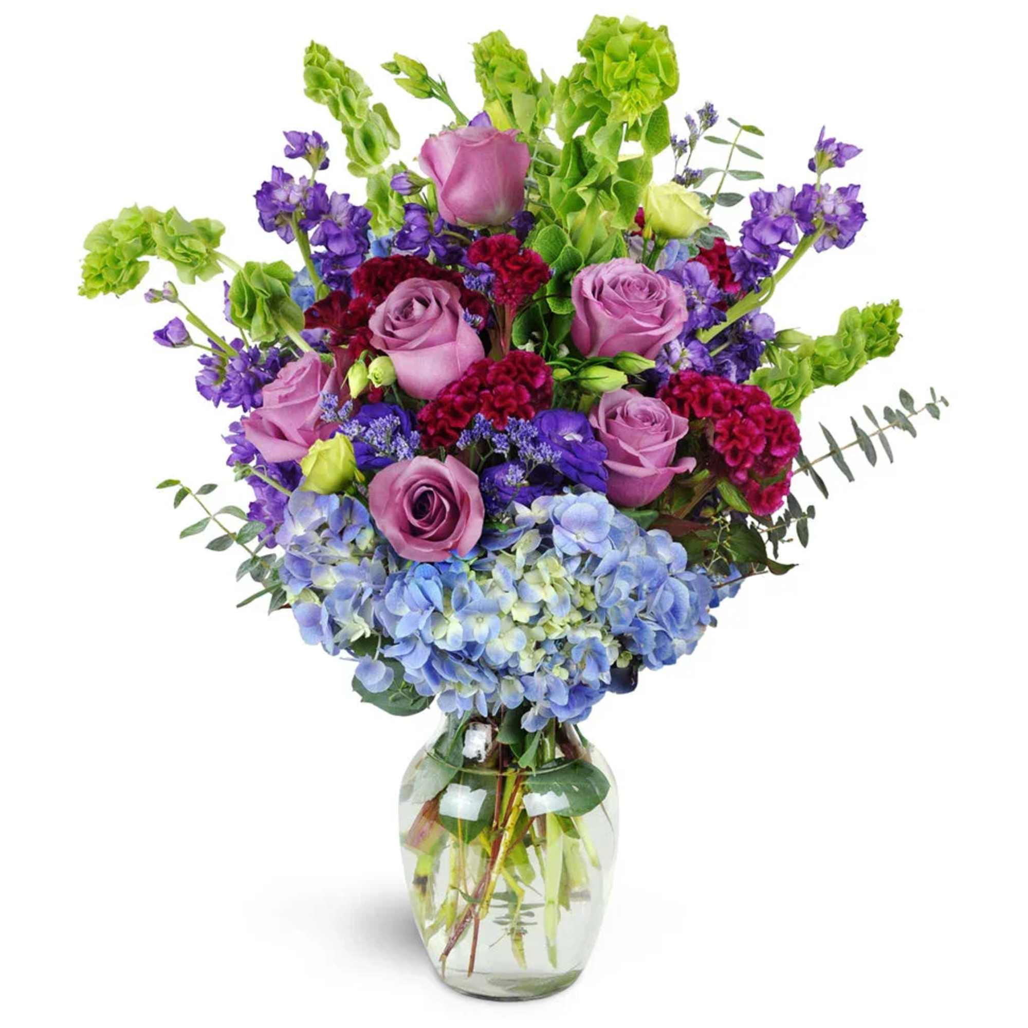 Mixed bouquet of purple roses, blue hydrangeas, and green blooms in a glass vase
