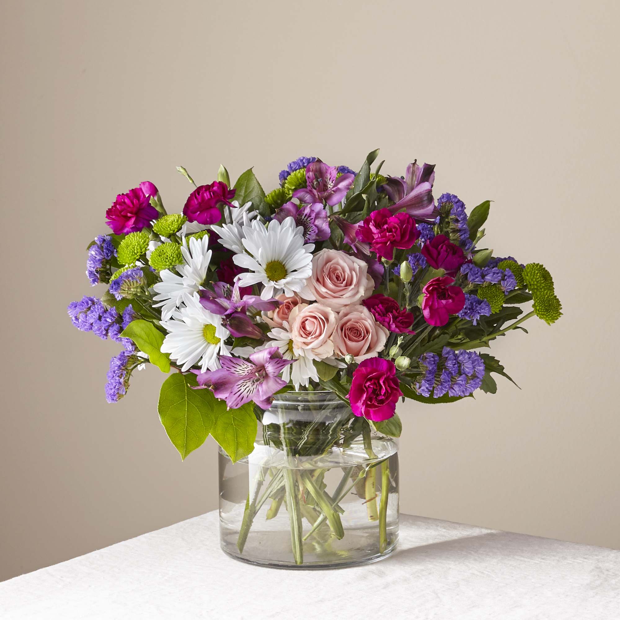 Mixed bouquet of daisies, roses, and purple flowers in a glass vase