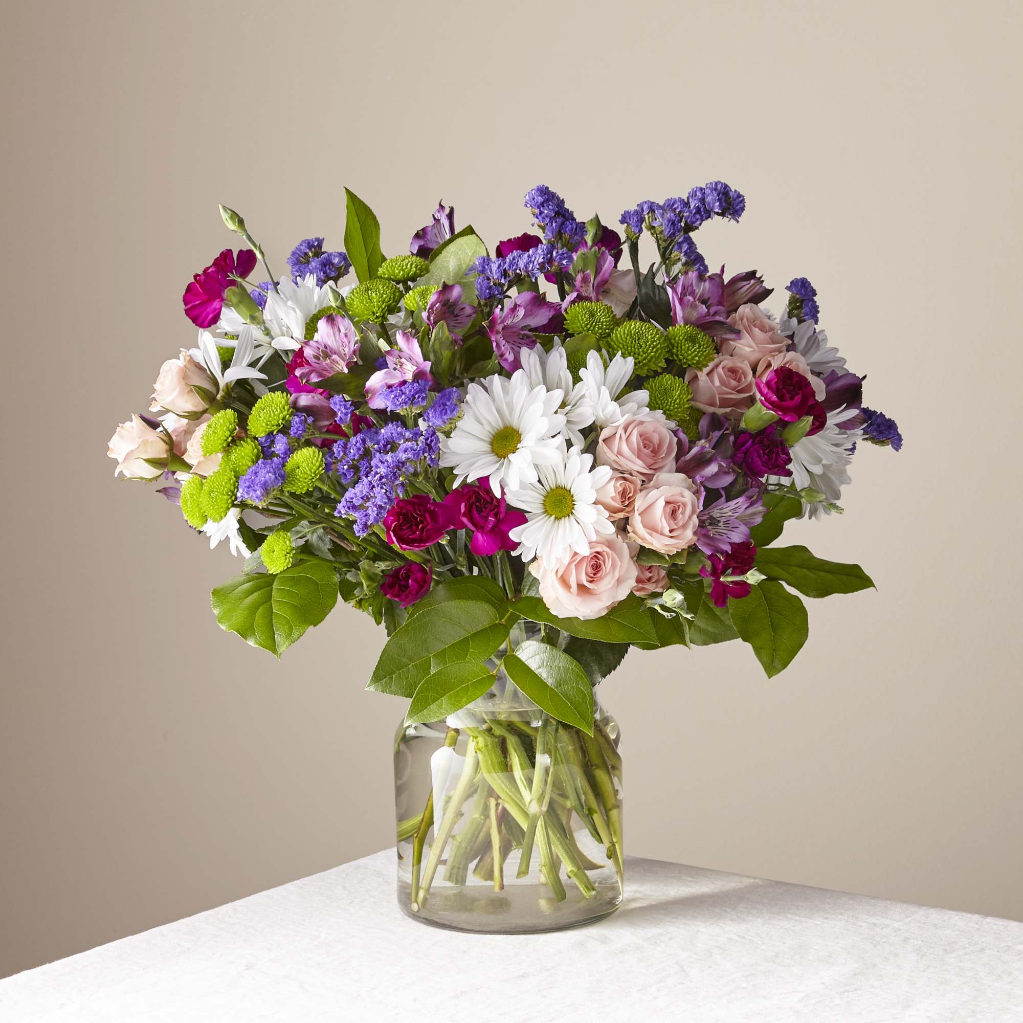 Mixed bouquet of roses, daisies, and purple flowers in a glass vase