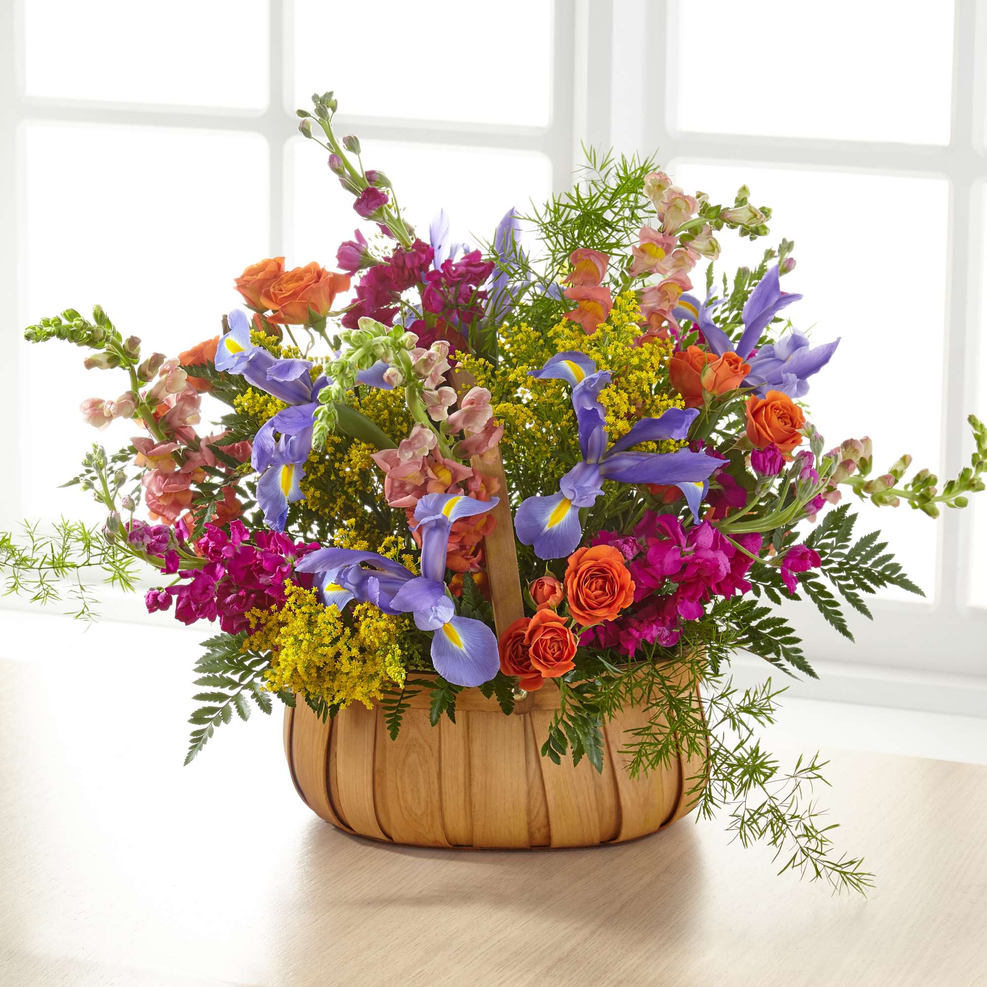 Mixed bouquet of orange roses, purple irises, and pink snapdragons in a wooden basket