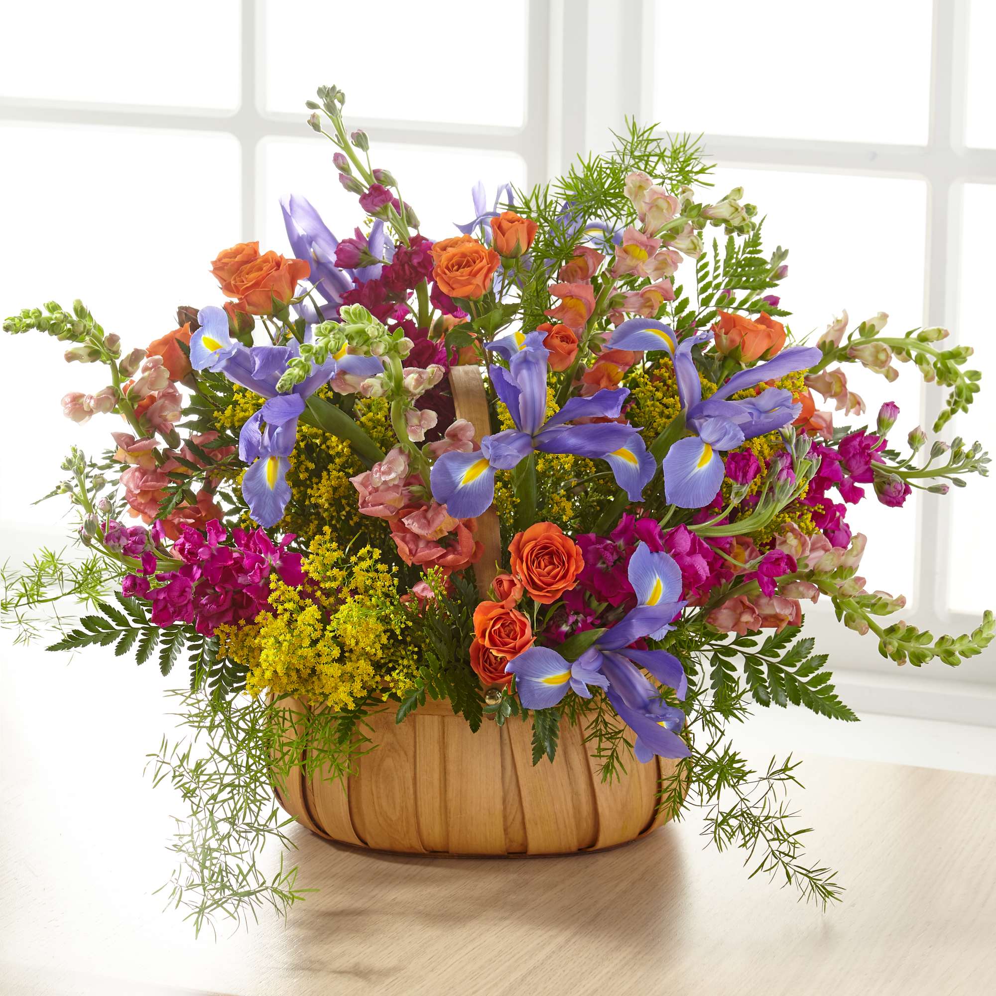 Mixed bouquet of orange roses, purple irises, and pink snapdragons in a wooden basket