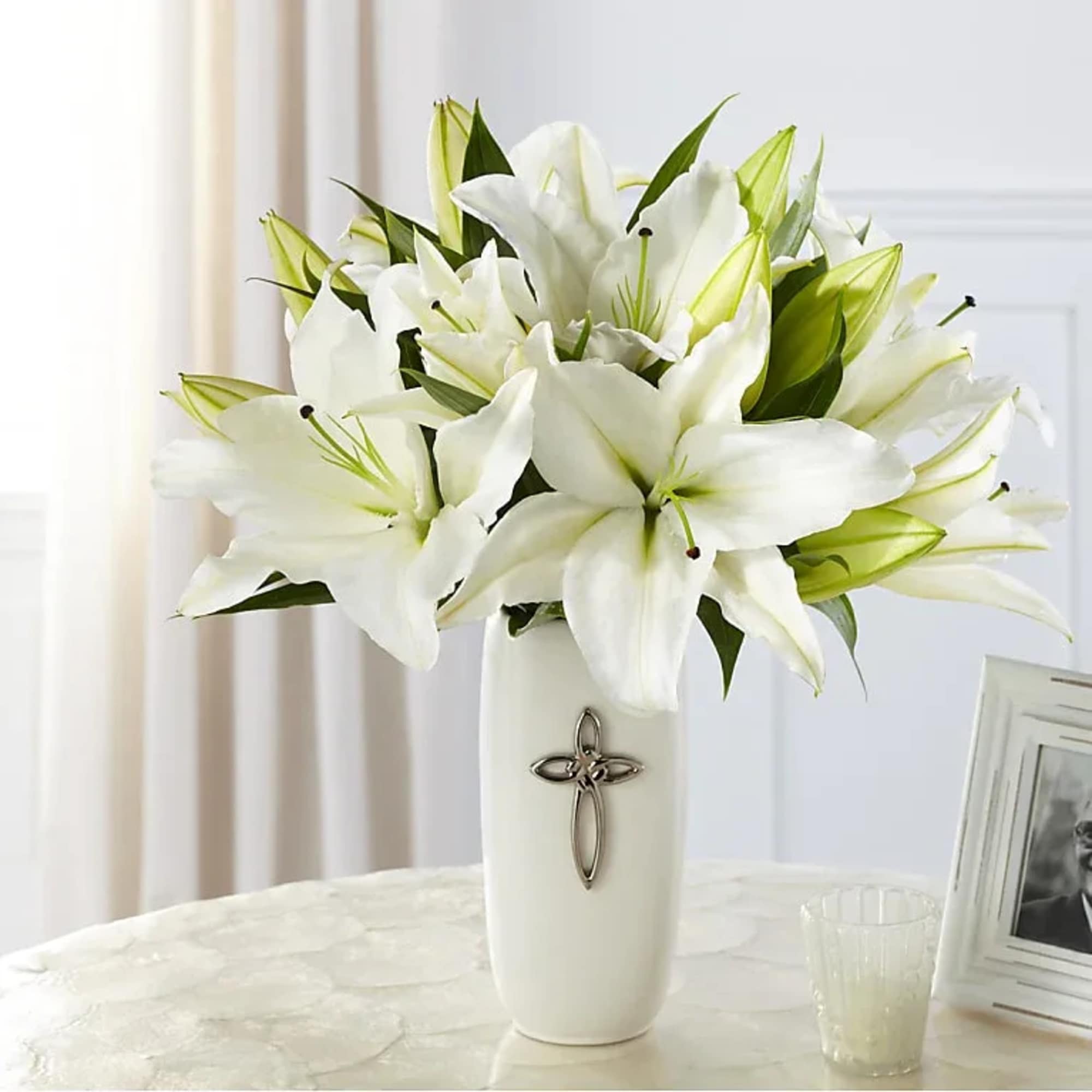 White lilies arranged in a white vase with a cross emblem