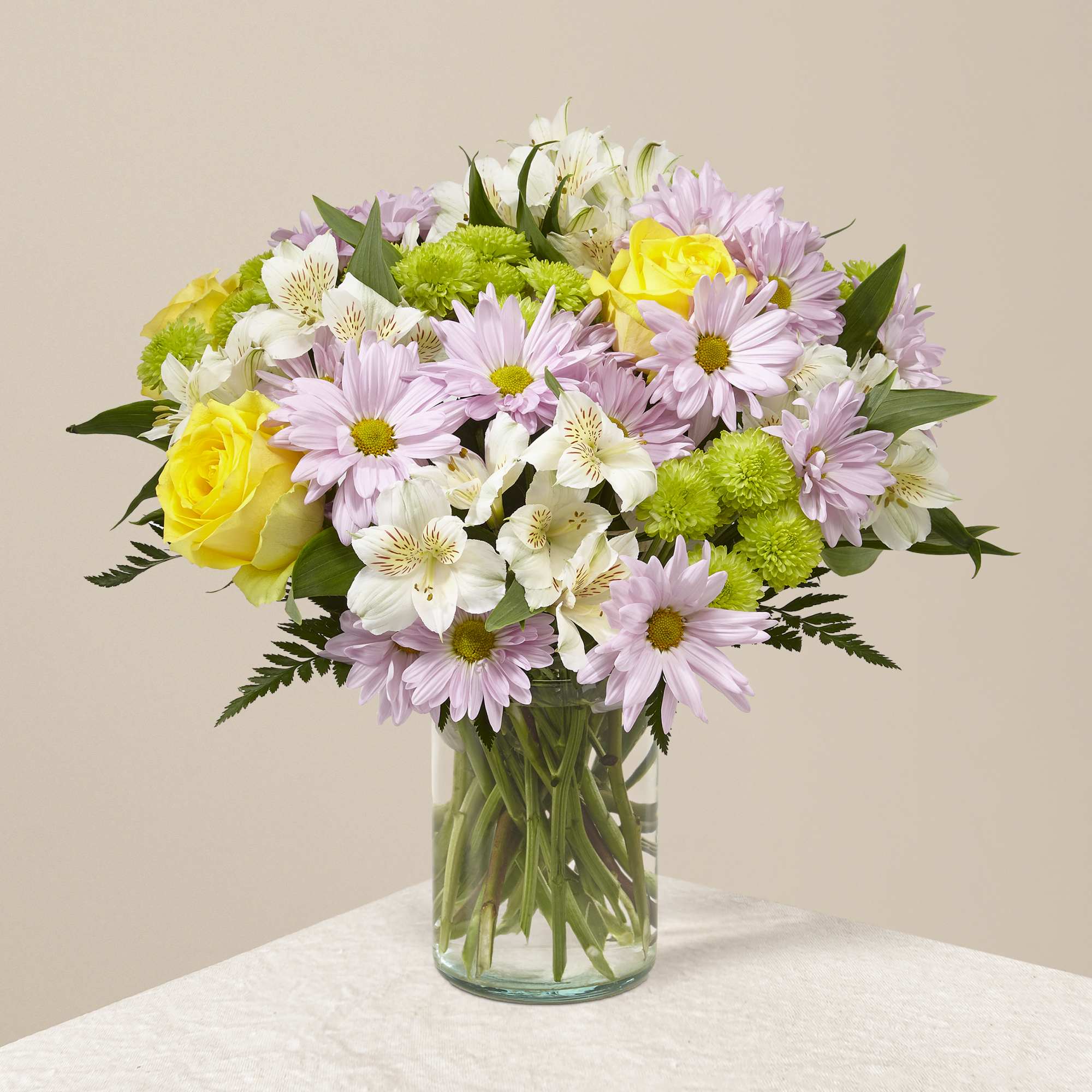Bouquet of pink daisies, yellow roses, and white alstroemeria in a glass vase