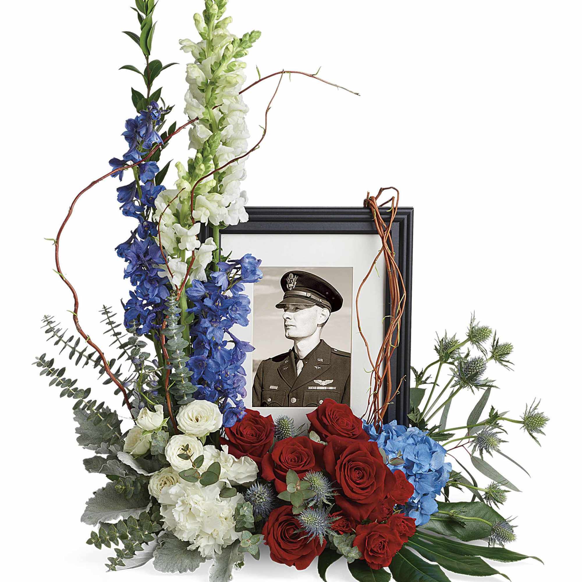 Floral tribute around a framed military portrait with red, white, and blue flowers