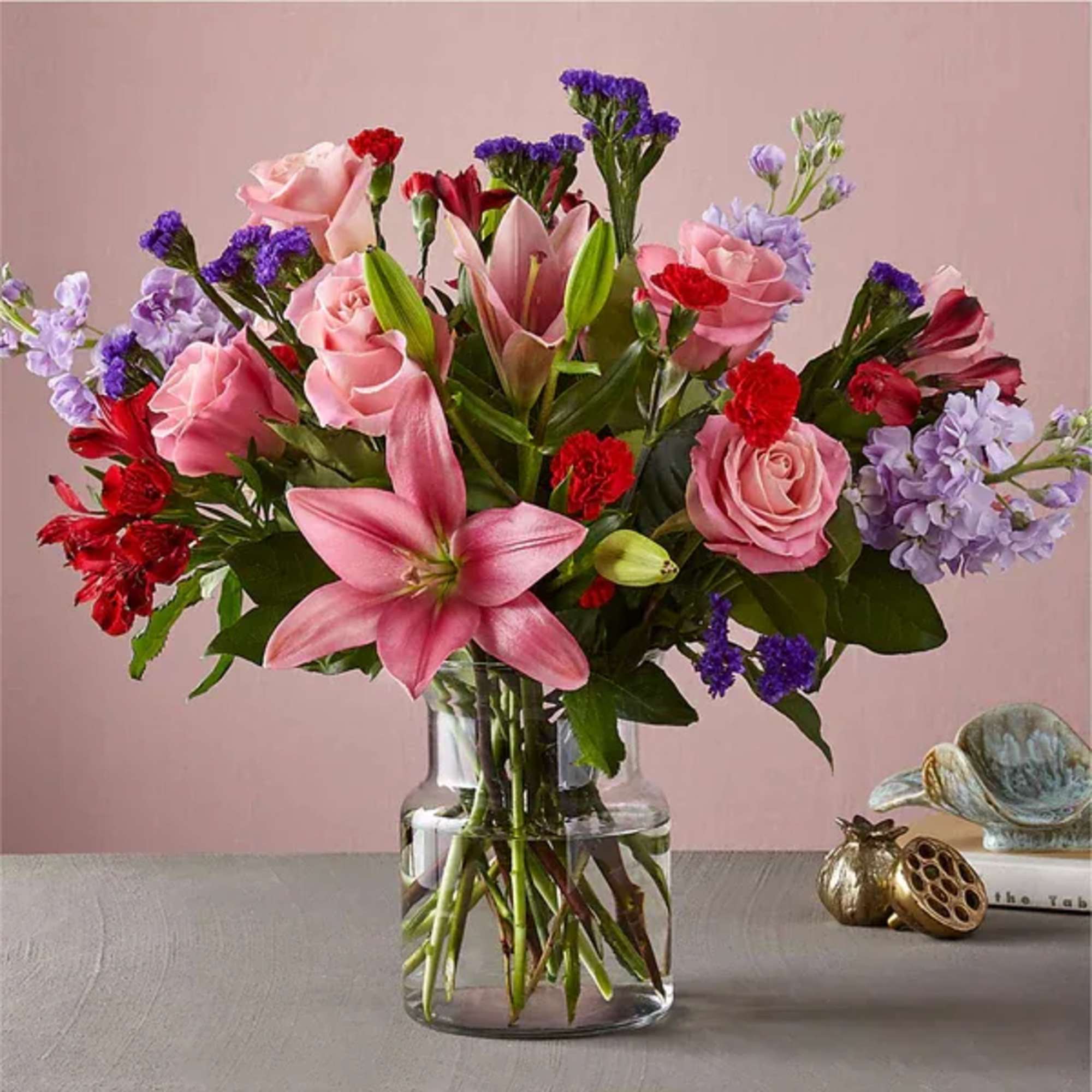 Pink lilies, roses, and purple flowers in a clear glass vase