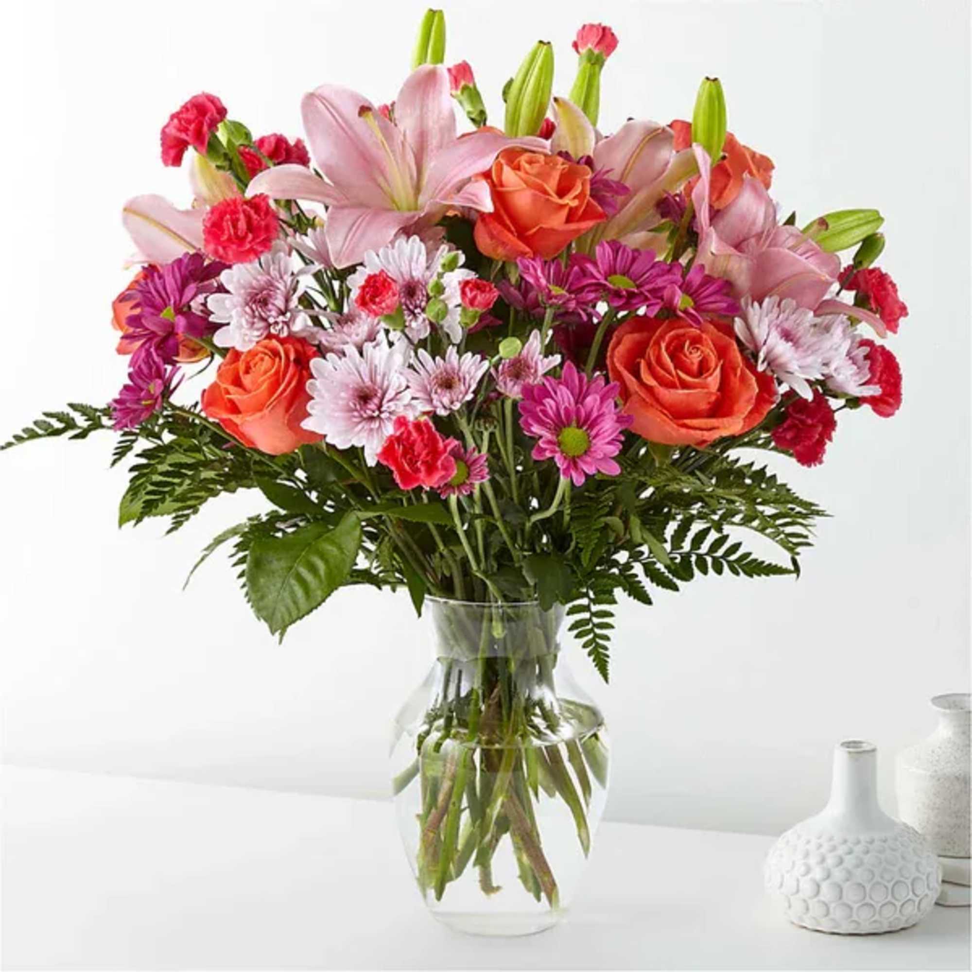 Mixed bouquet of pink lilies, orange roses, and daisies in a glass vase