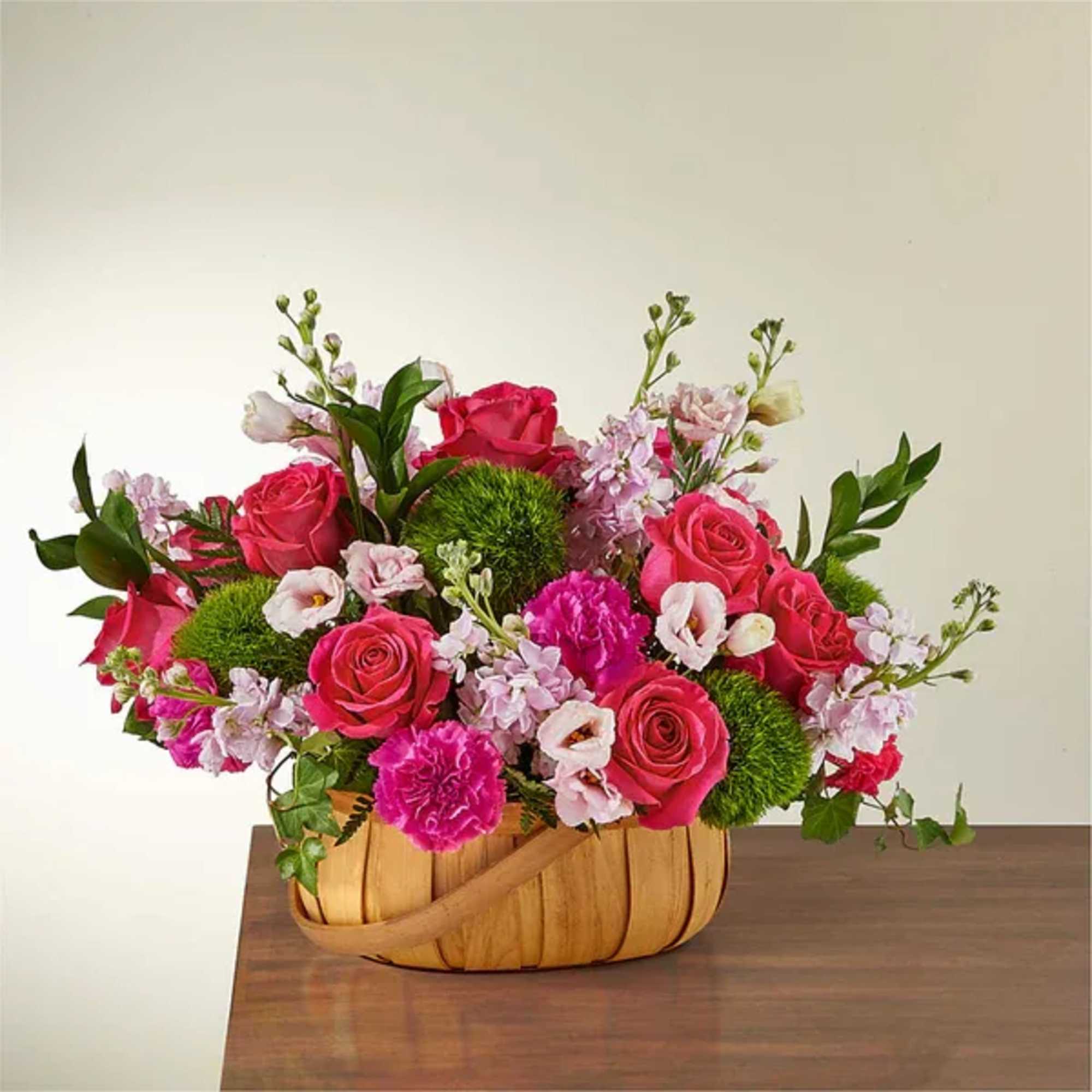 Pink roses and carnations arranged in a woven basket.