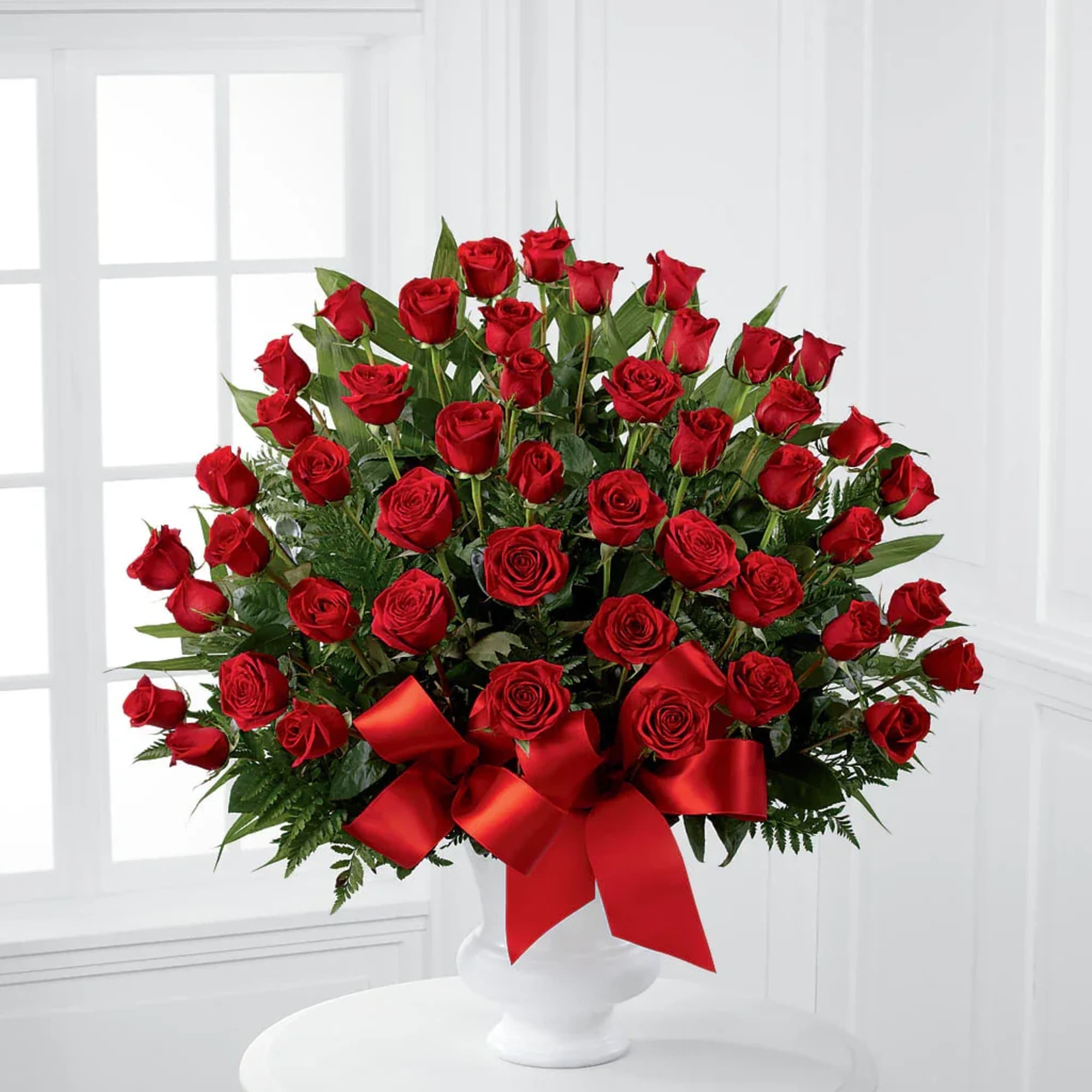Large bouquet of red roses in a white vase with a red ribbon