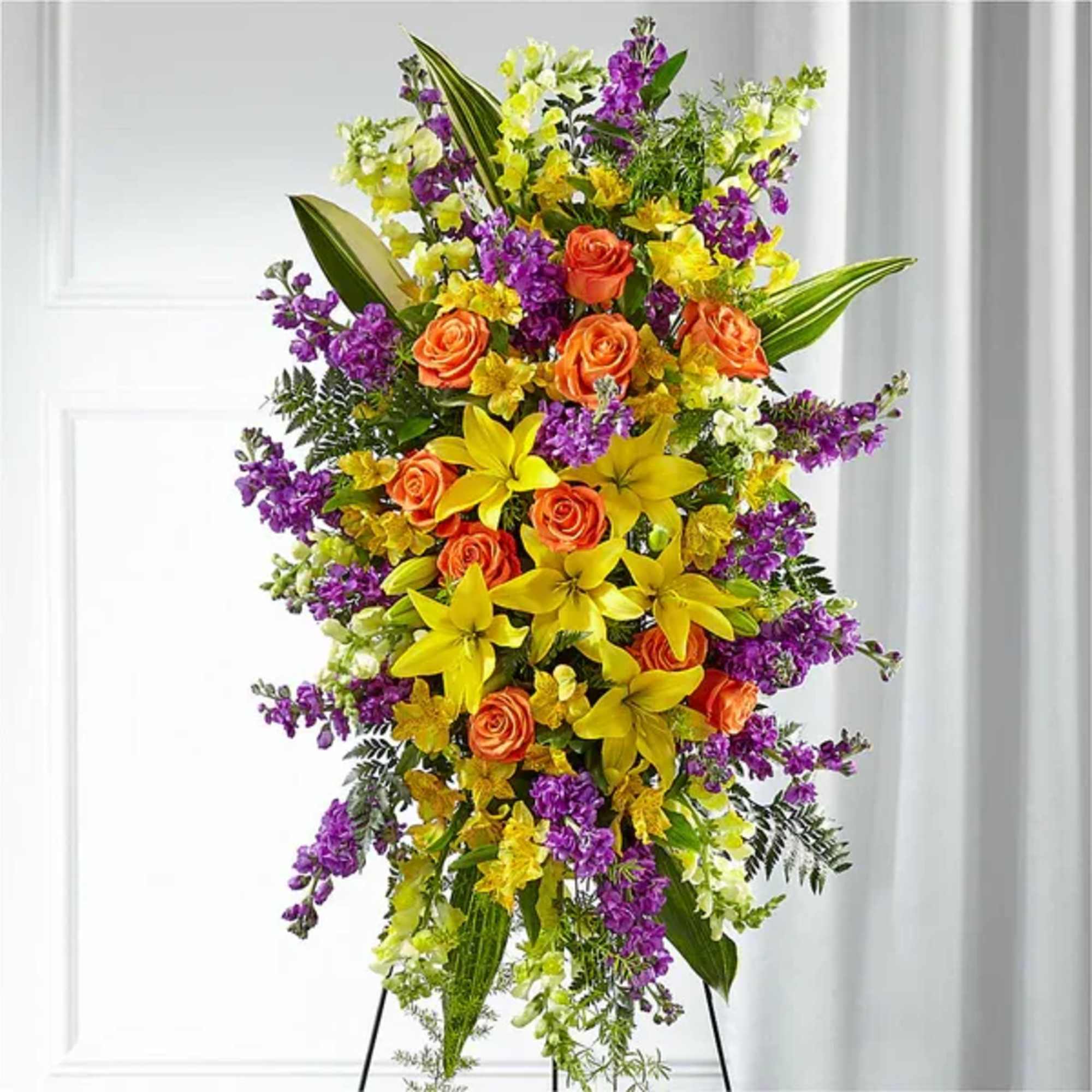 Tall floral standing spray with orange roses, yellow lilies, and purple blooms
