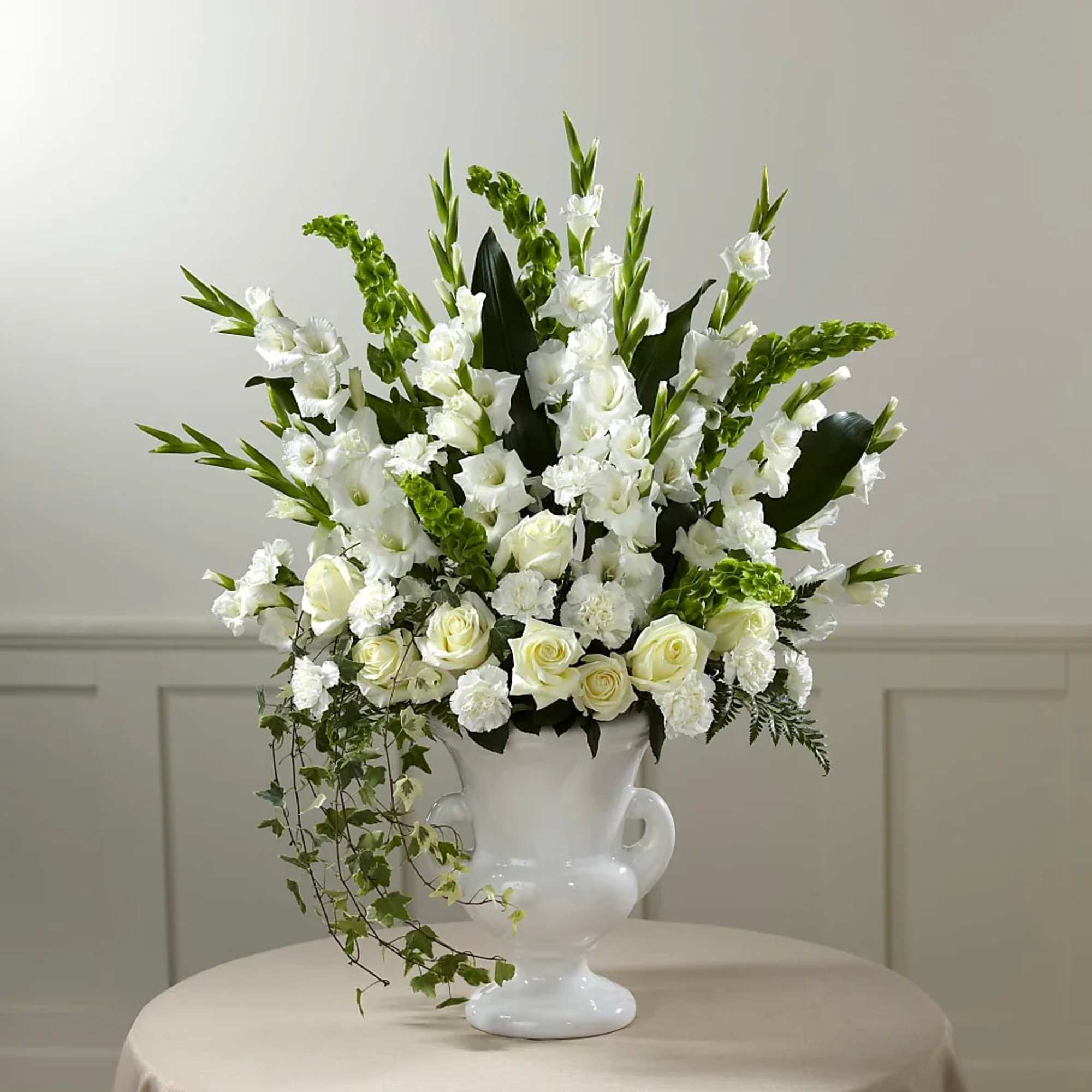 White floral arrangement in a white urn vase with trailing greenery
