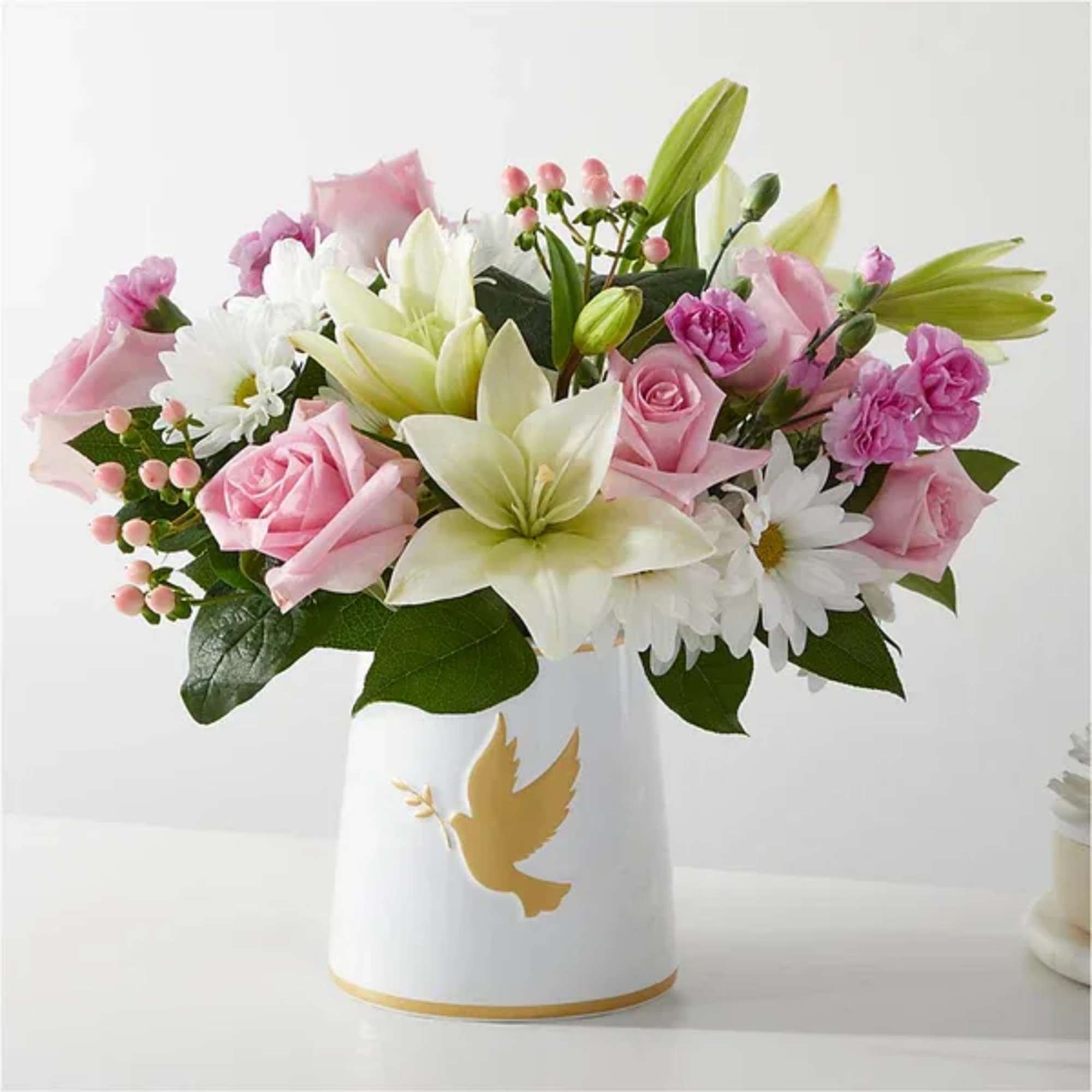 Pink and white flower arrangement in a white vase with a gold dove design