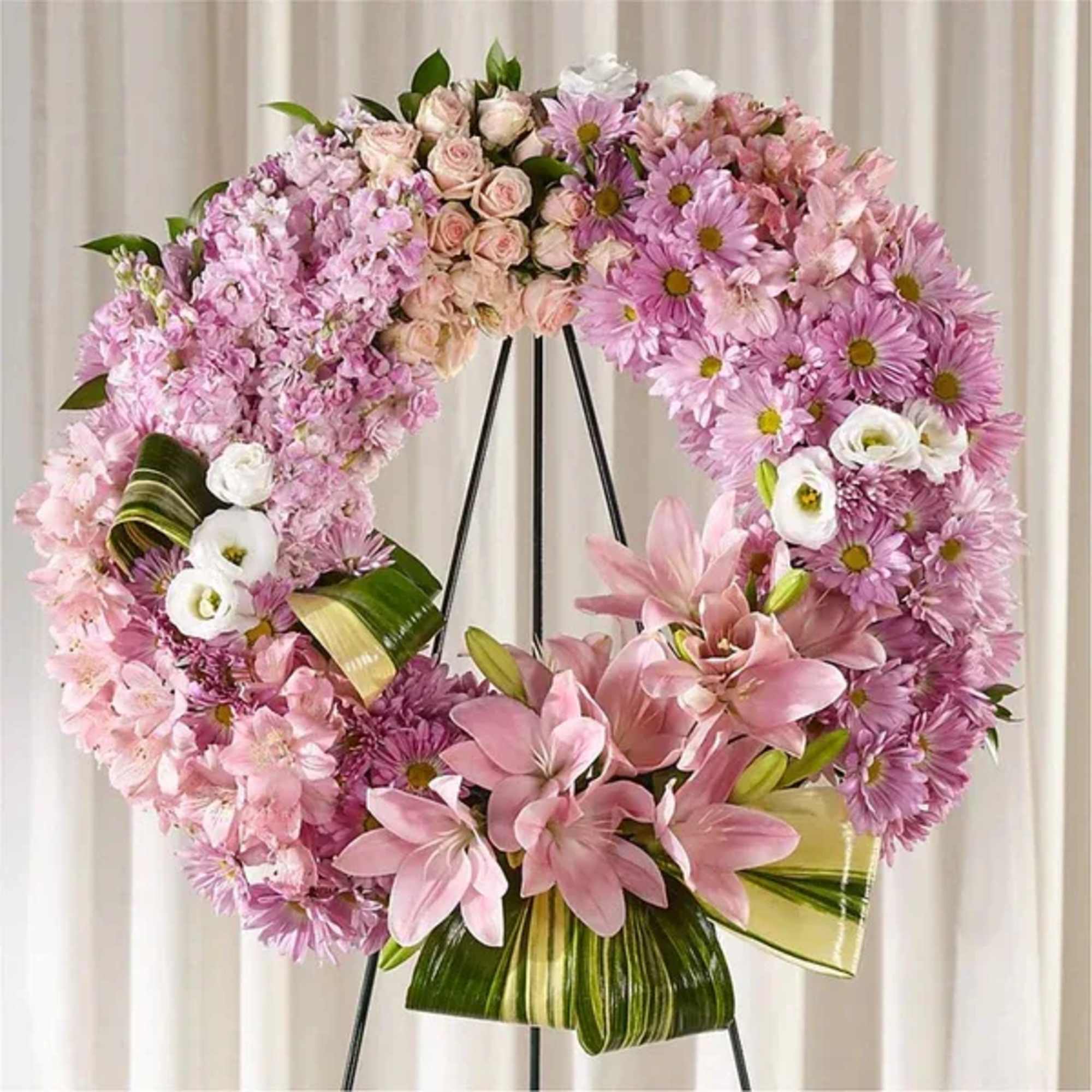 Pink floral wreath with lilies and daisies on a black stand