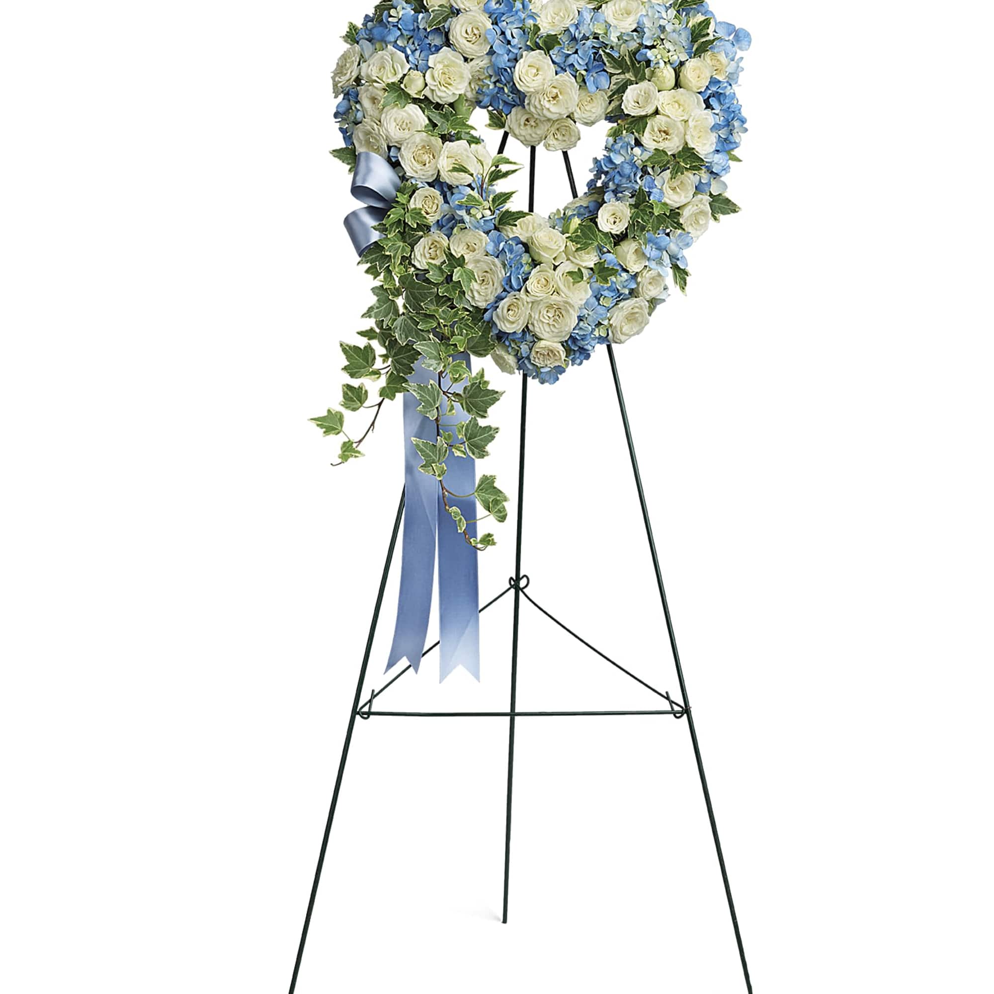 Heart-shaped floral wreath on a stand with white roses and blue flowers