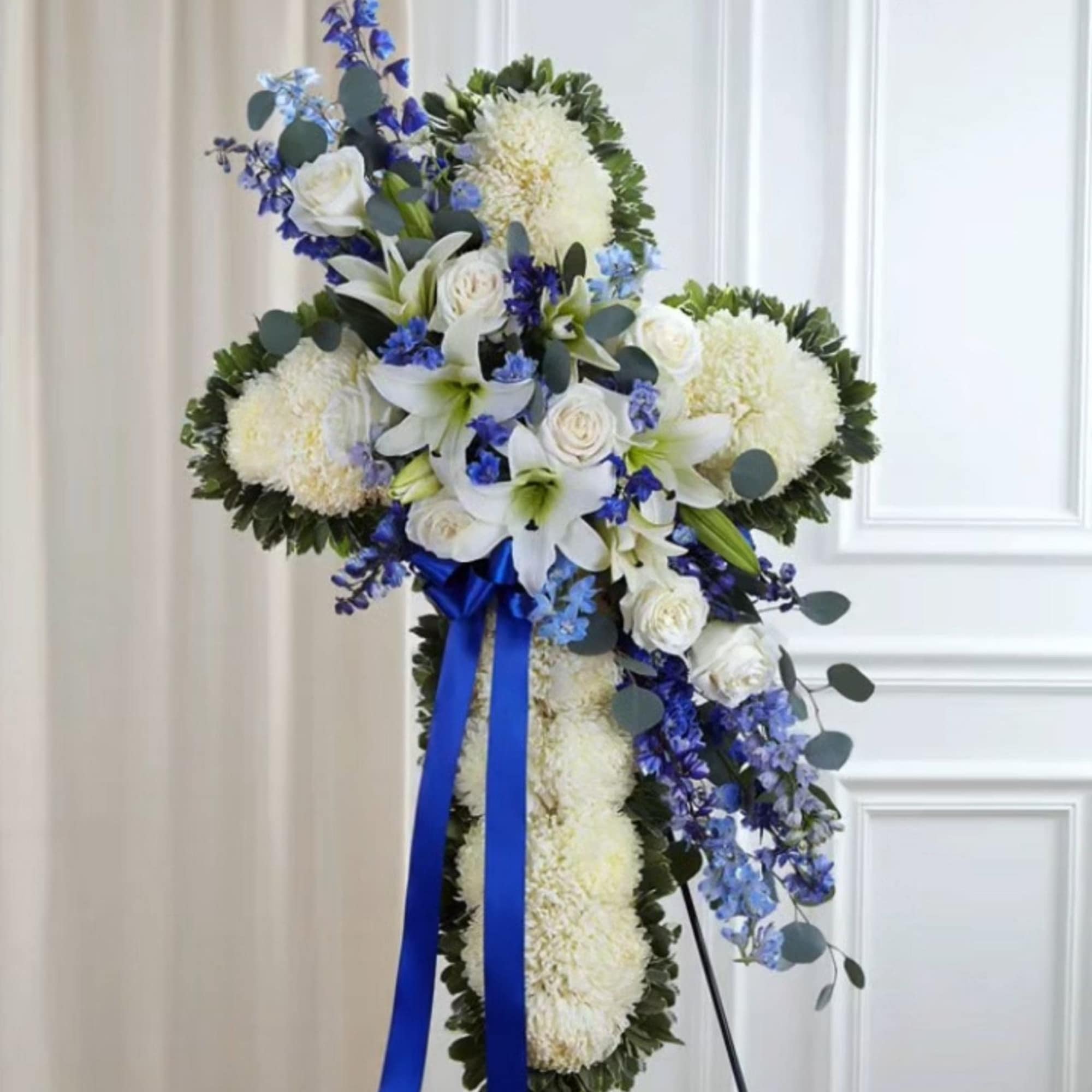 White and blue funeral spray with lilies and roses on a stand