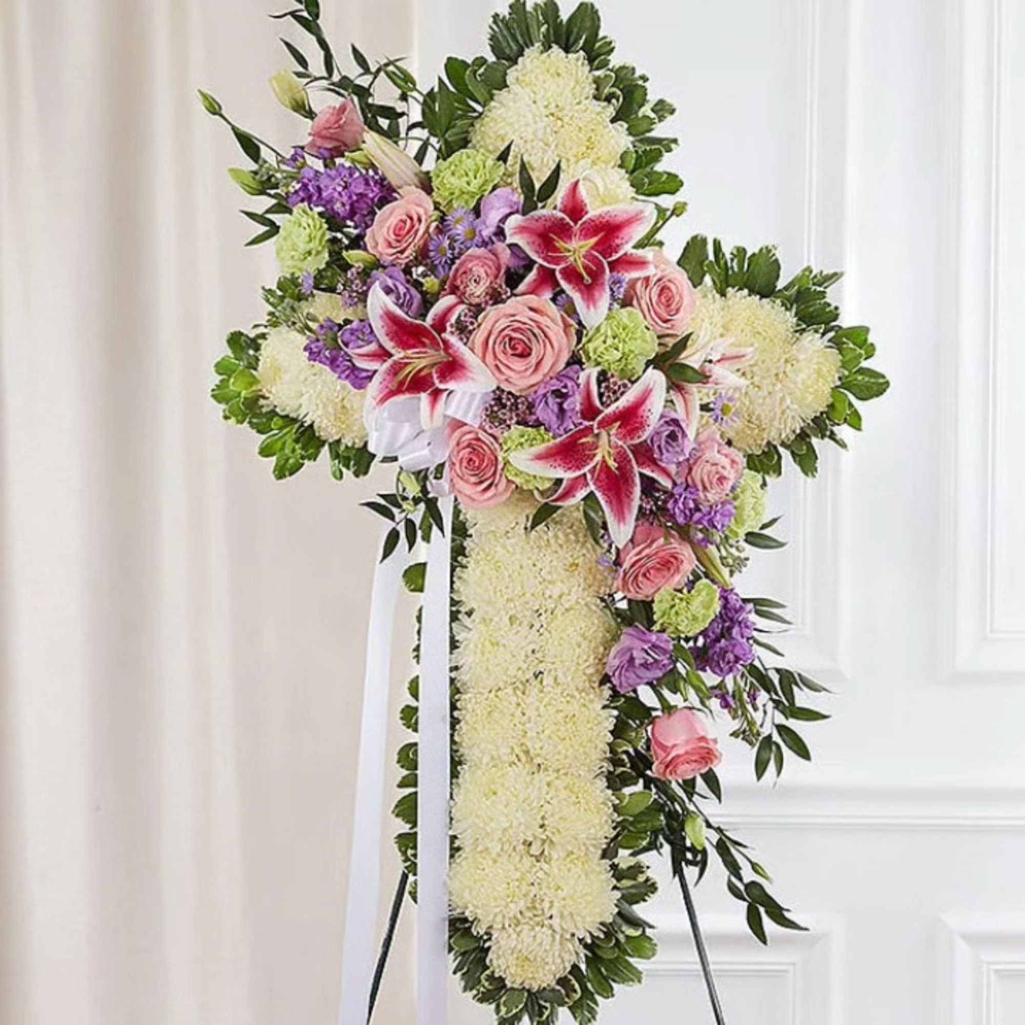Cross-shaped floral spray with pink roses and lilies on a stand