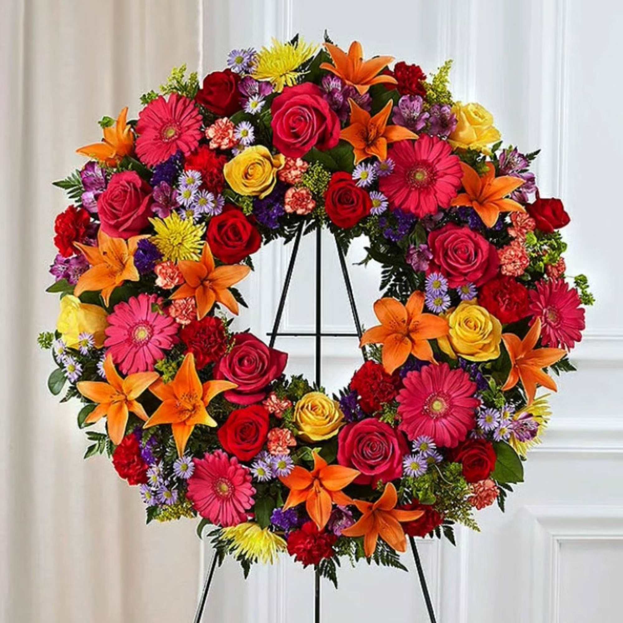 Colorful floral wreath on a black stand with roses, lilies, and daisies