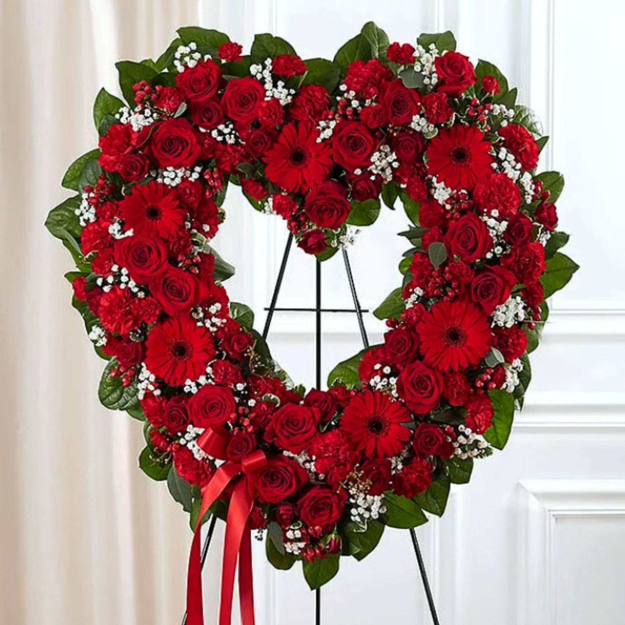 Heart-shaped red flower wreath on a stand with a ribbon