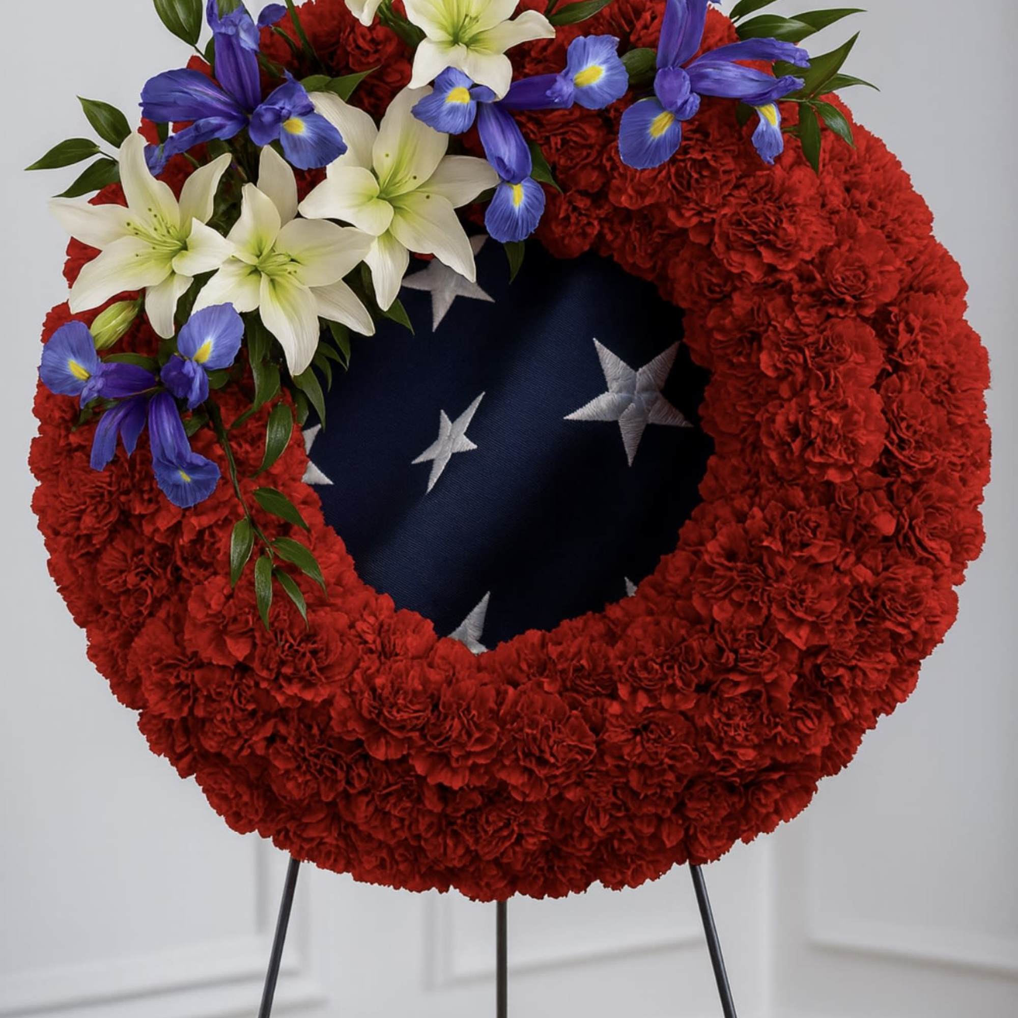 Red floral wreath with white lilies and blue flowers on a stand