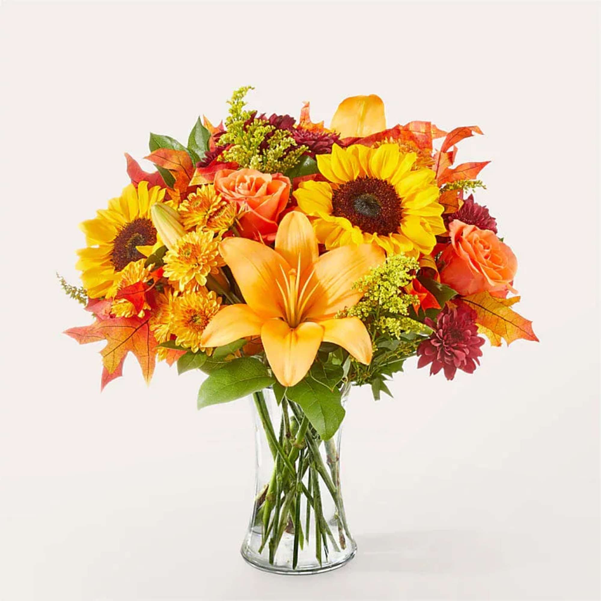 Autumn bouquet with sunflowers, lilies, roses, and mums in a glass vase