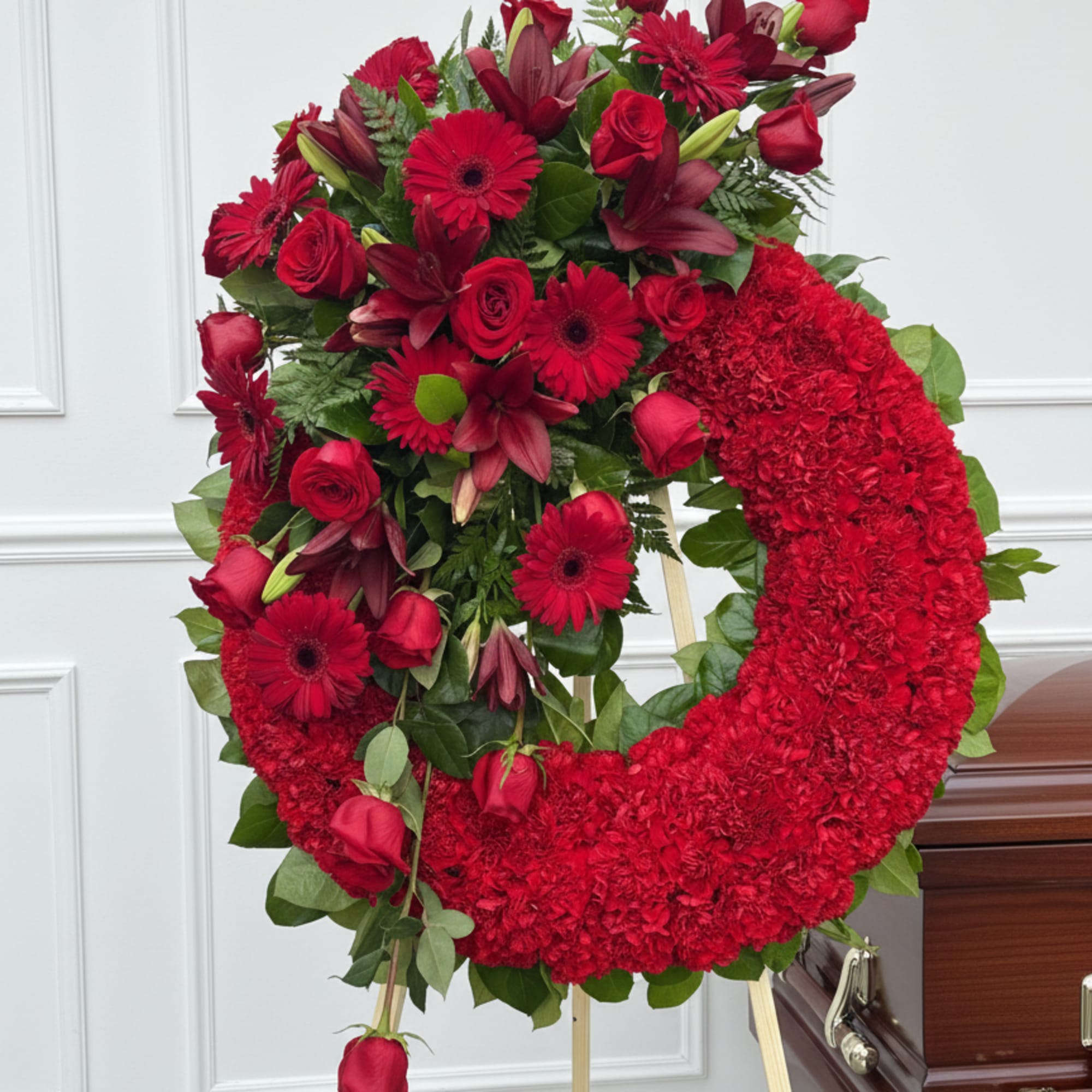 Red floral funeral wreath on a standing easel beside a casket