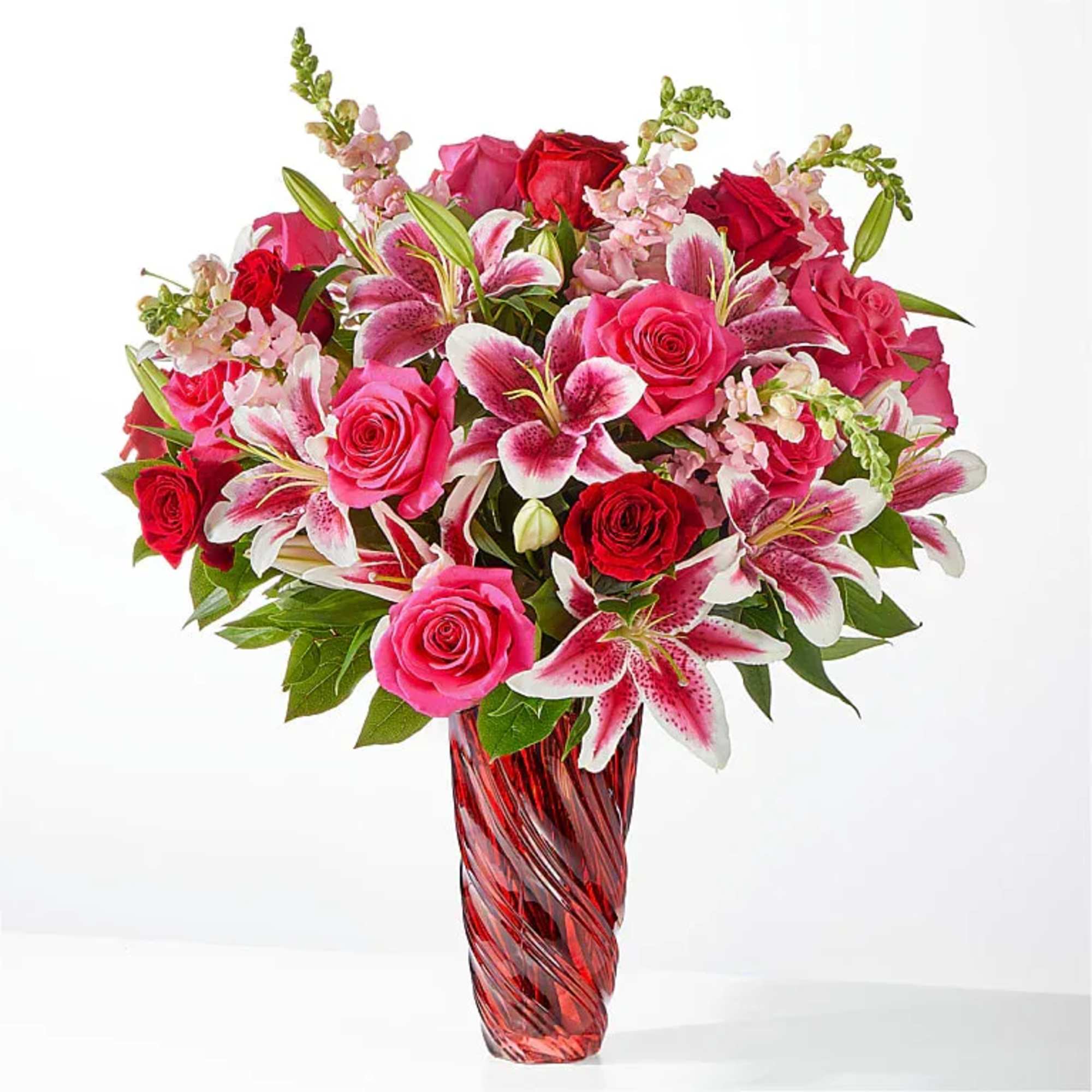 Pink and red roses with lilies in a red glass vase