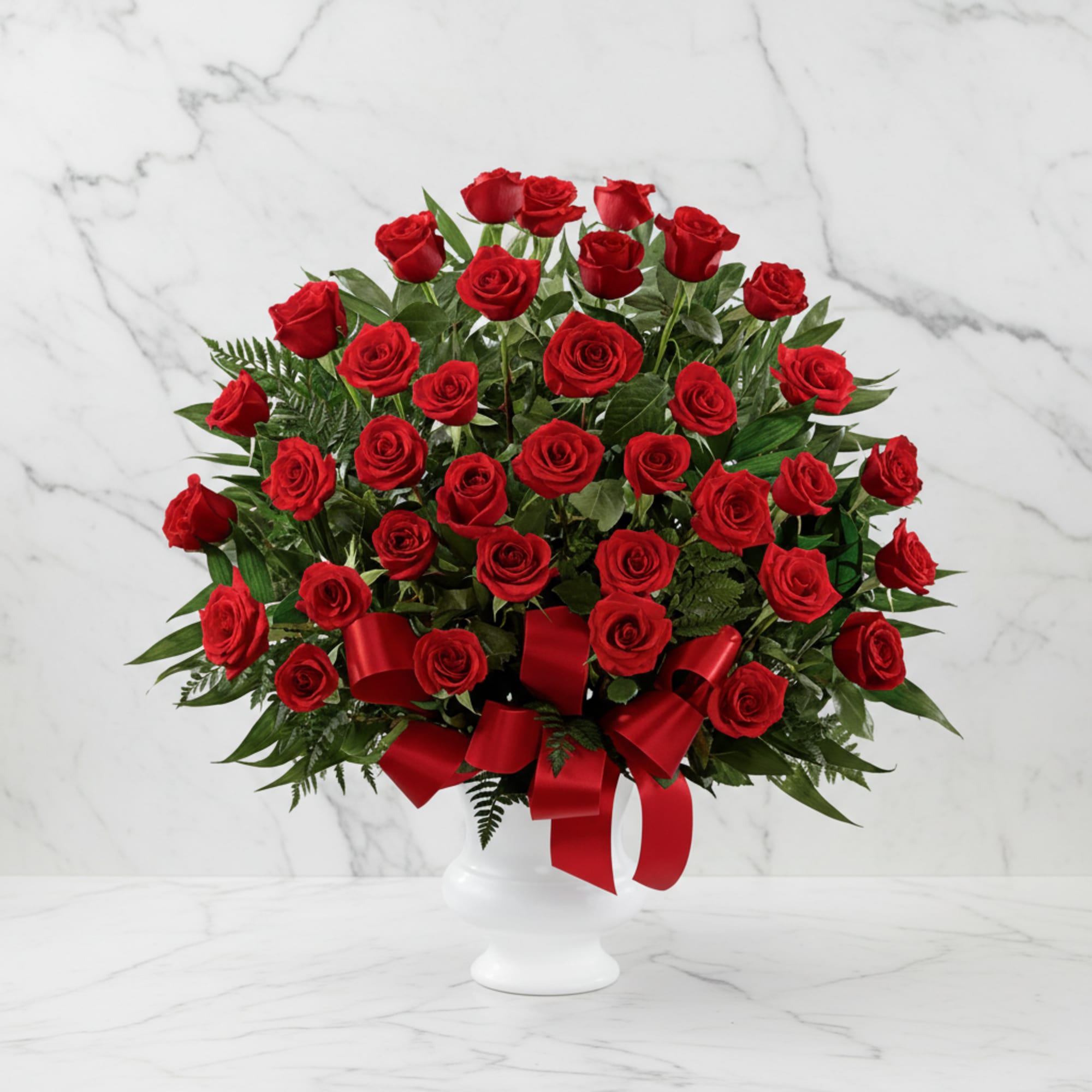 Red roses arranged in a white vase with a red ribbon