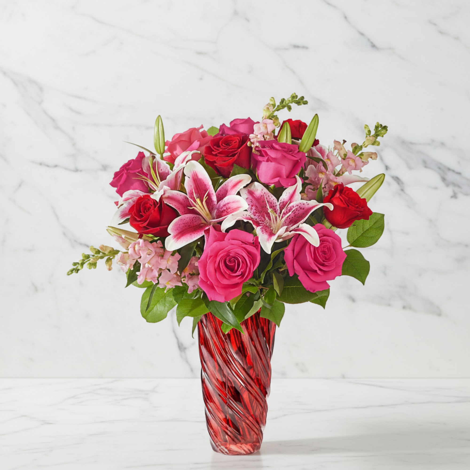 Pink and red roses with lilies in a red glass vase