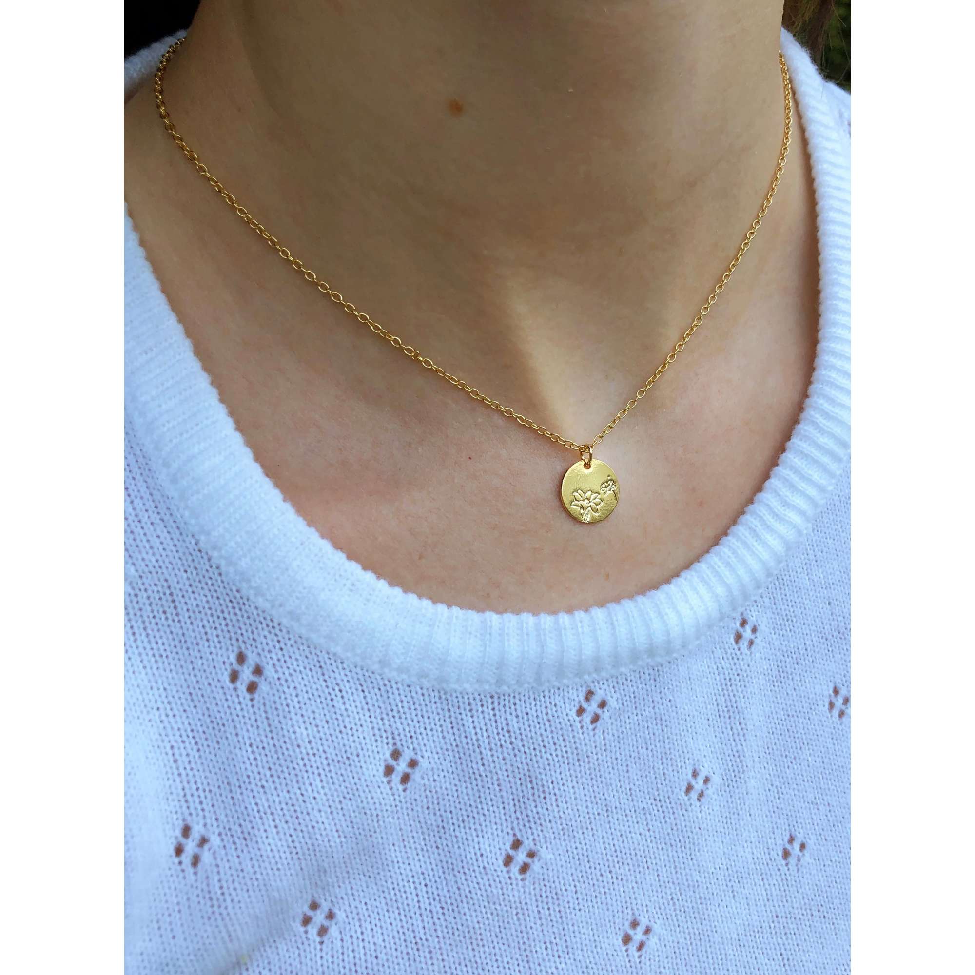 Gold necklace with a small round pendant worn over a white sweater