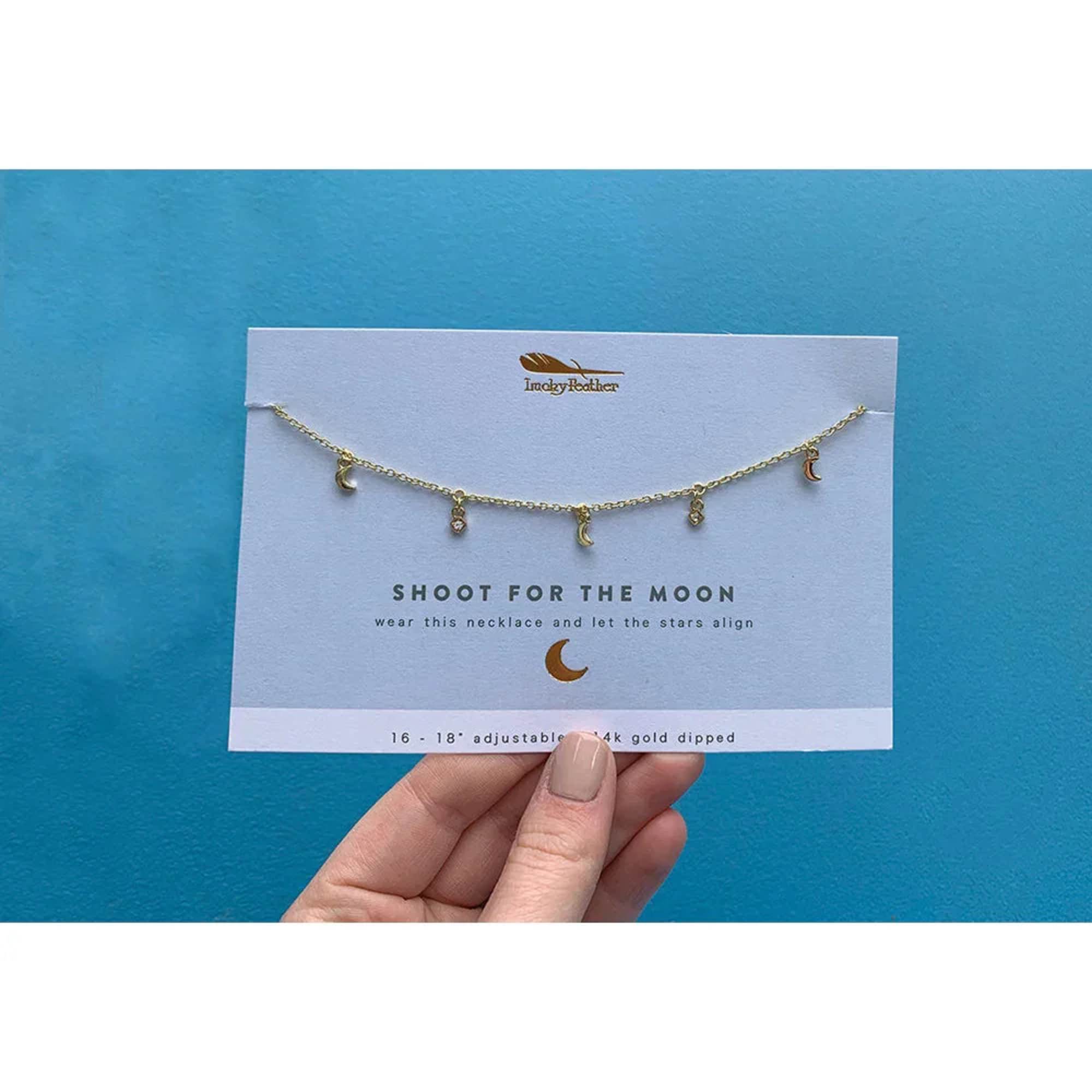 Hand holding a card with a gold moon charm necklace