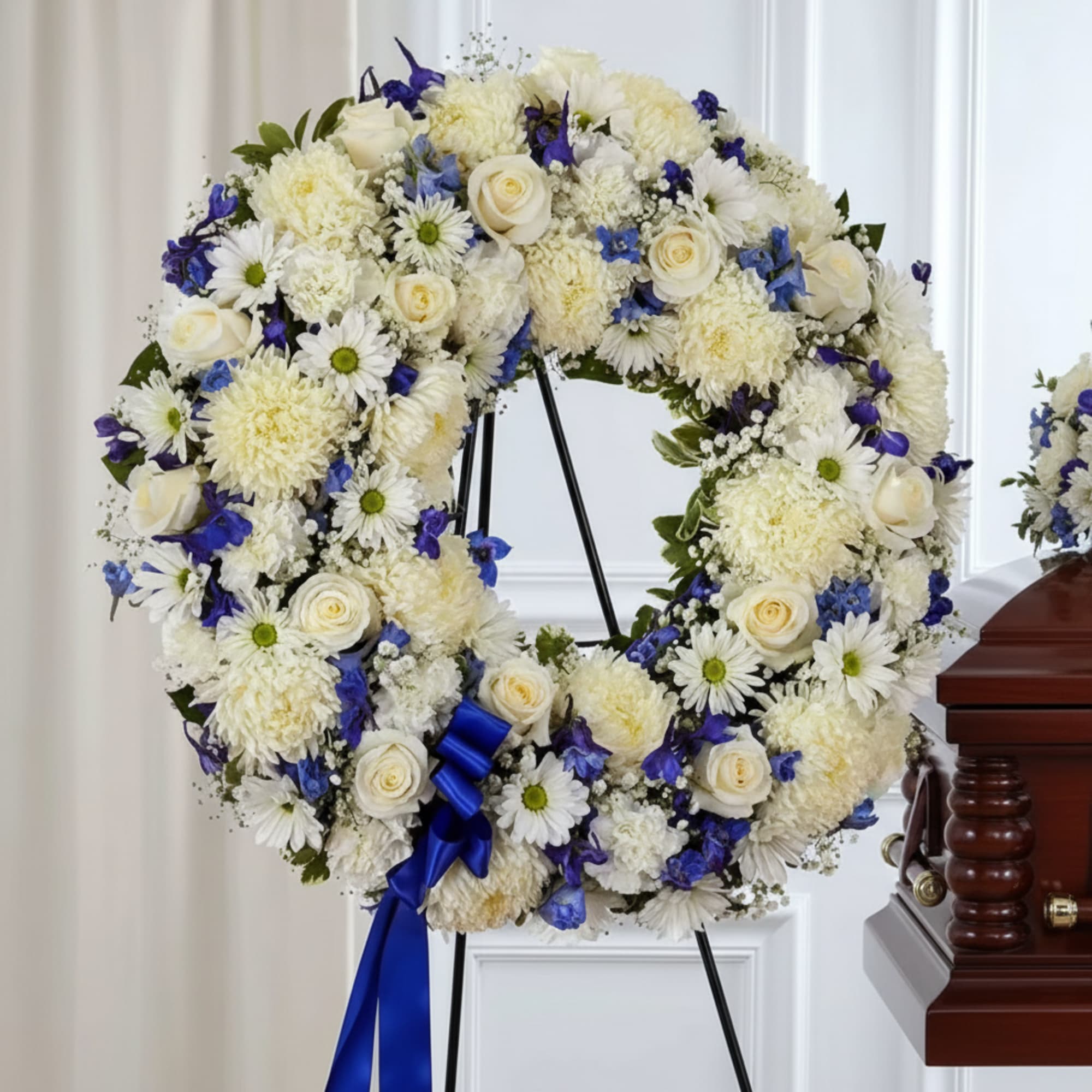 White and blue floral wreath on a stand with a blue ribbon