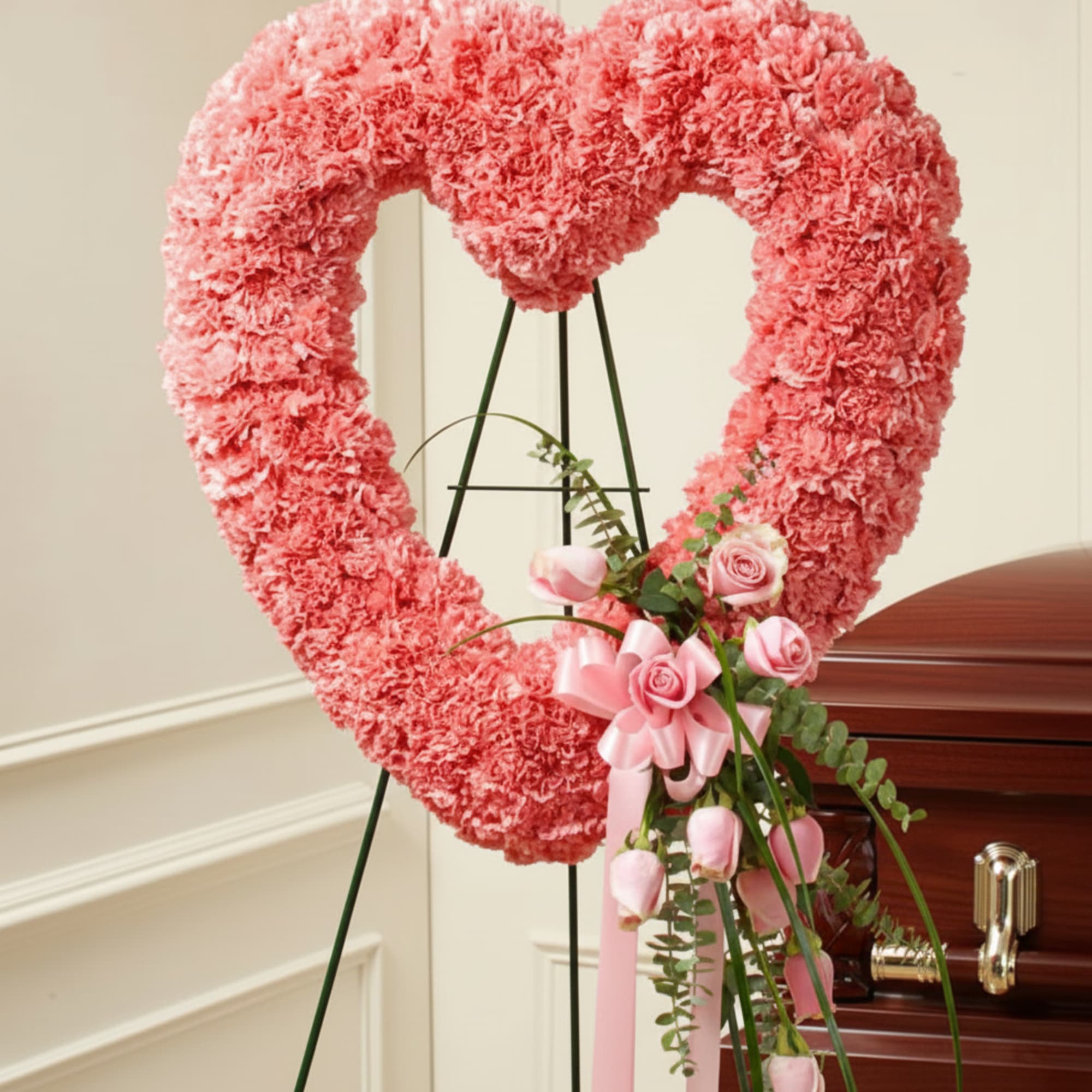 Pink heart-shaped floral funeral tribute on a stand with roses and ribbon