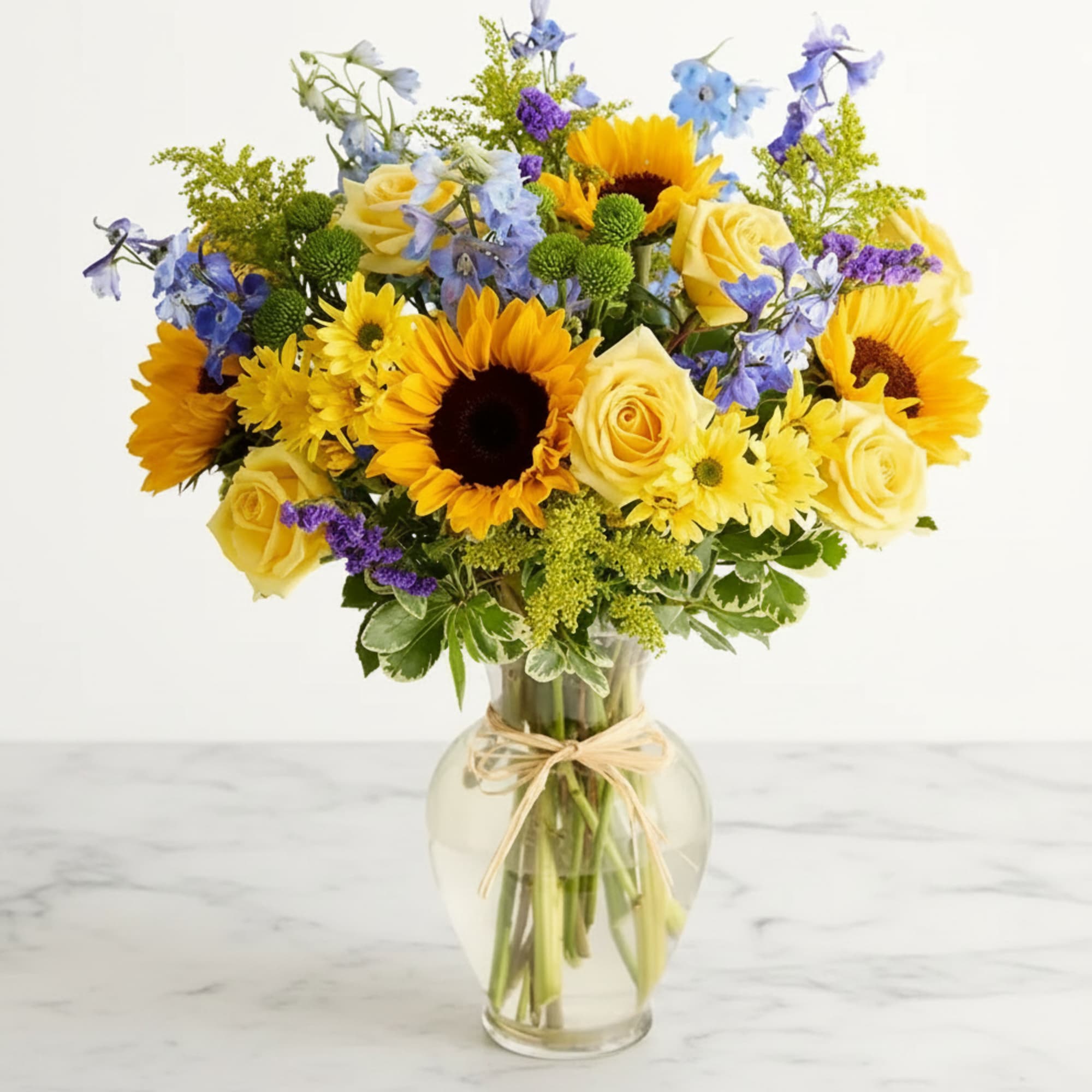 Bouquet of sunflowers, yellow roses, and blue flowers in a glass vase