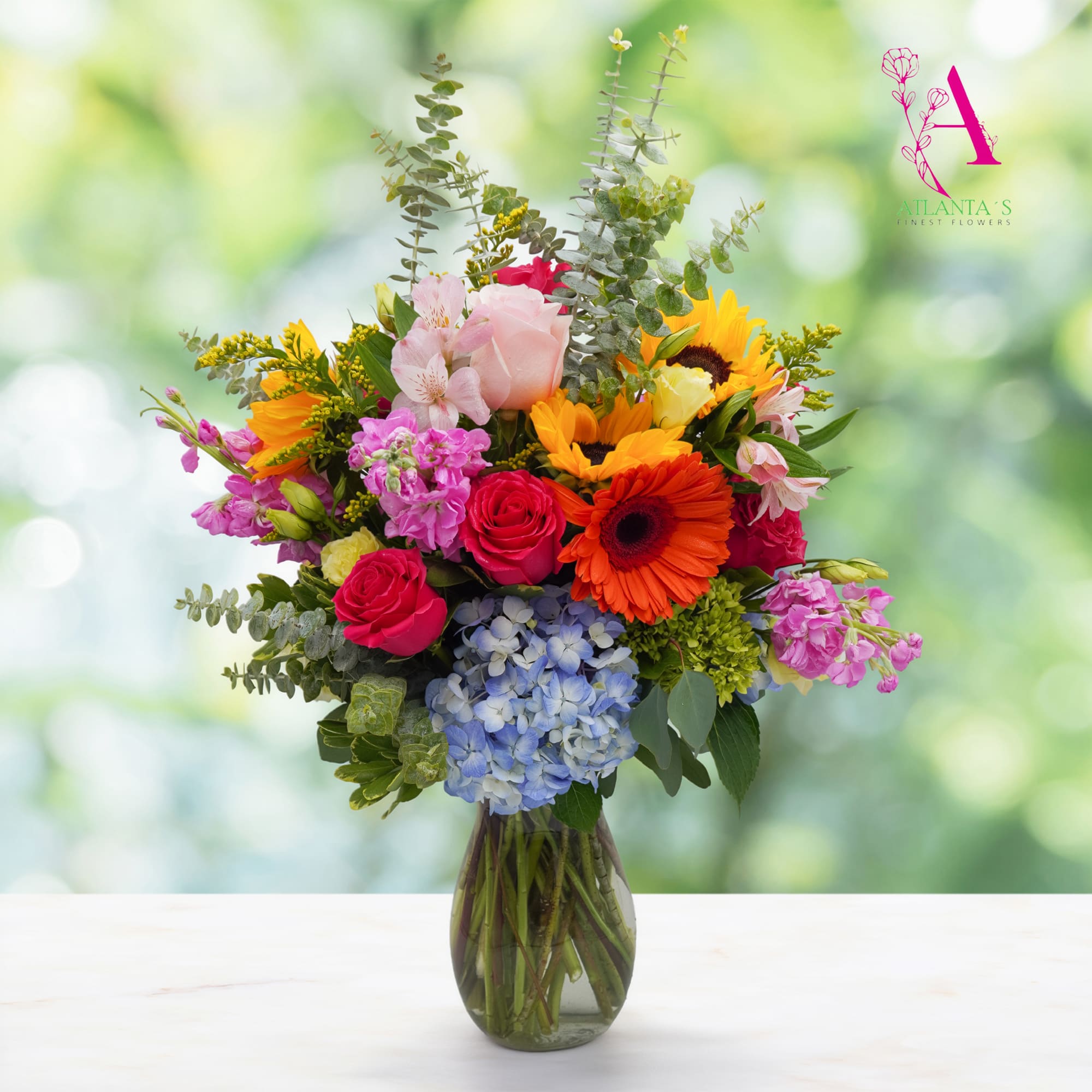 Colorful mixed bouquet in a glass vase with roses, gerbera daisies, hydrangea, and sunflowers