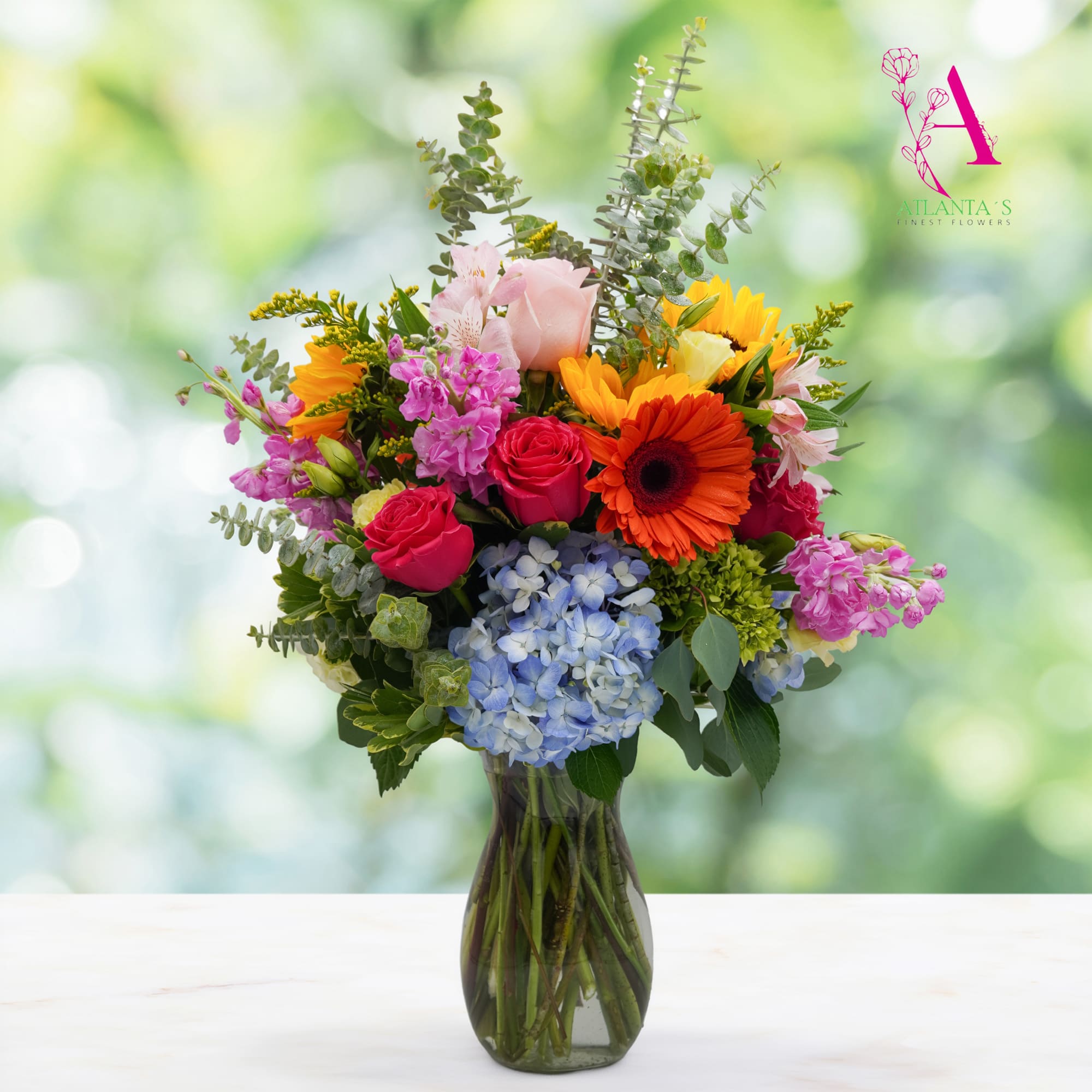 Mixed bouquet of roses, gerbera daisies, hydrangeas, and pink blooms in a glass vase