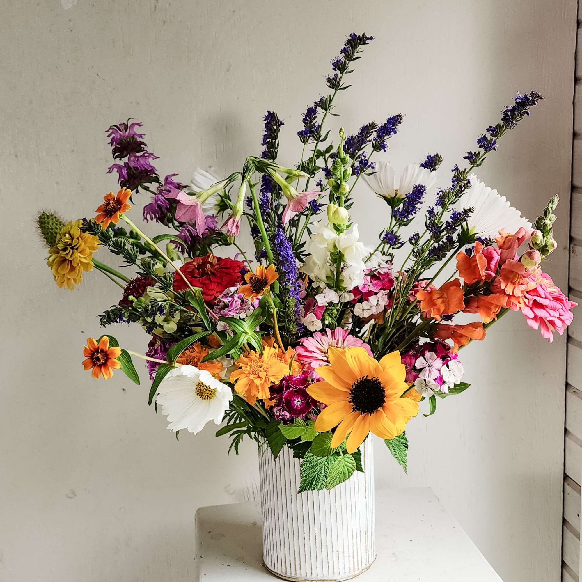 Mixed bouquet in a white ribbed vase with sunflowers and daisies