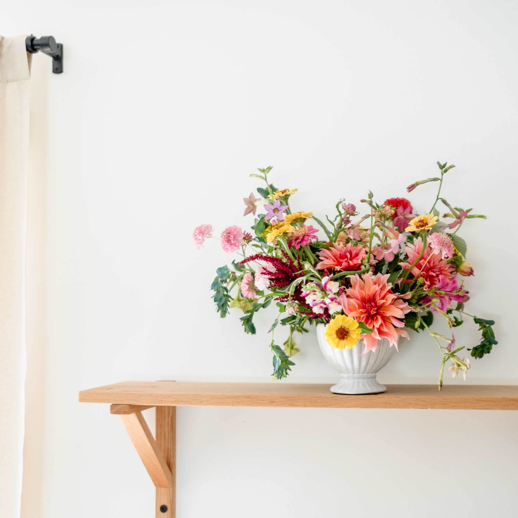 Colorful mixed flower arrangement in a white vase on a wooden shelf
