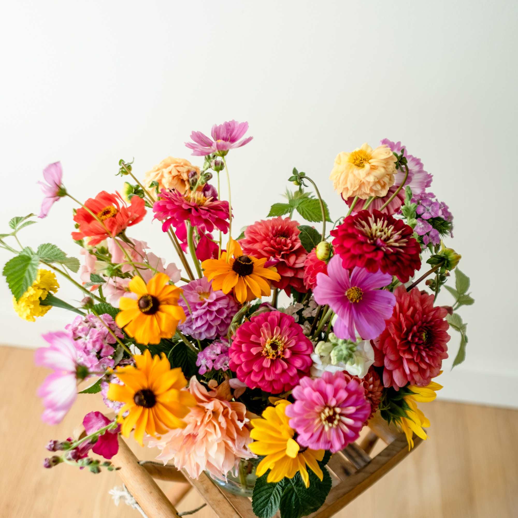 Colorful mixed flower bouquet in a glass vase on a wooden stool