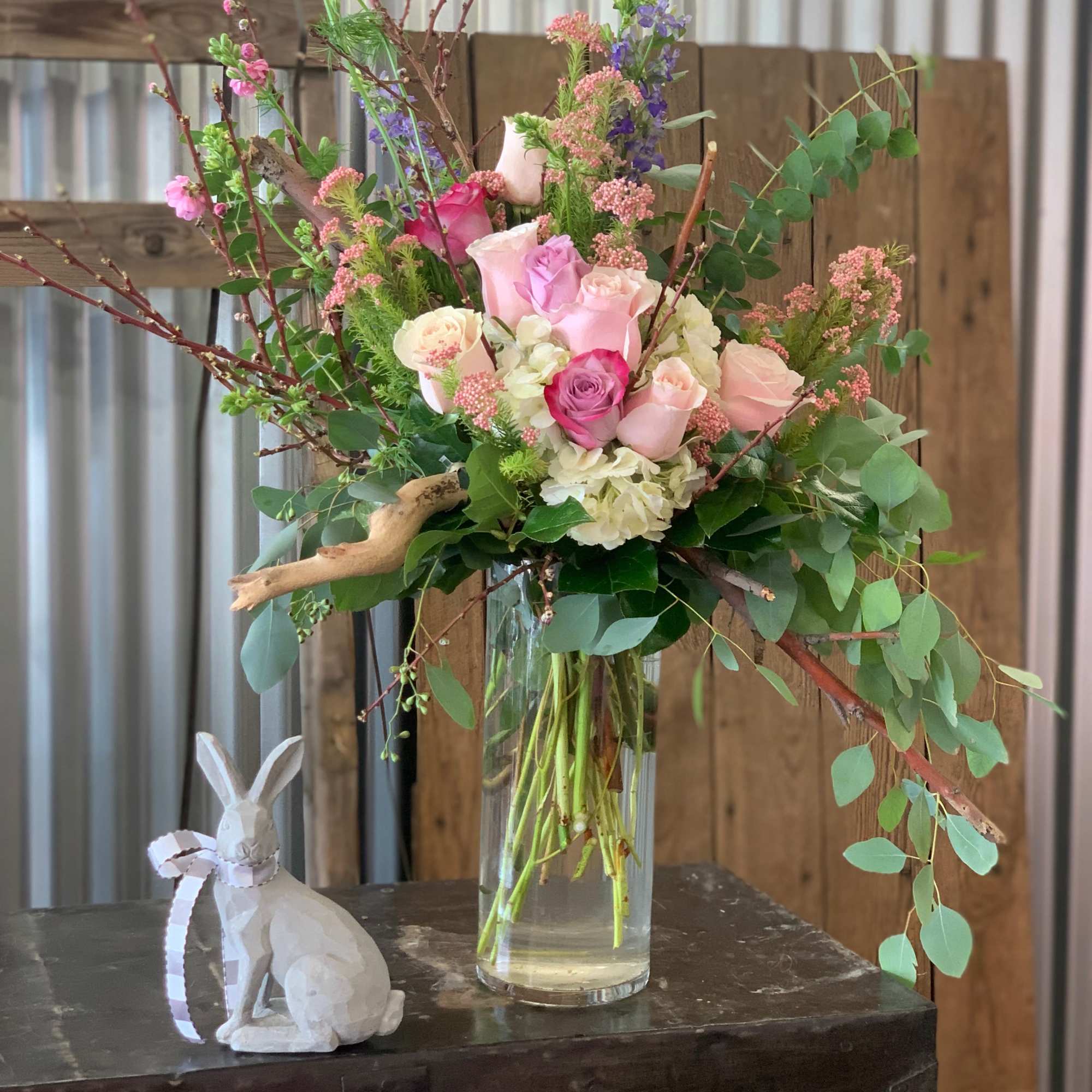 Pink and white roses in a tall glass vase with eucalyptus and branches