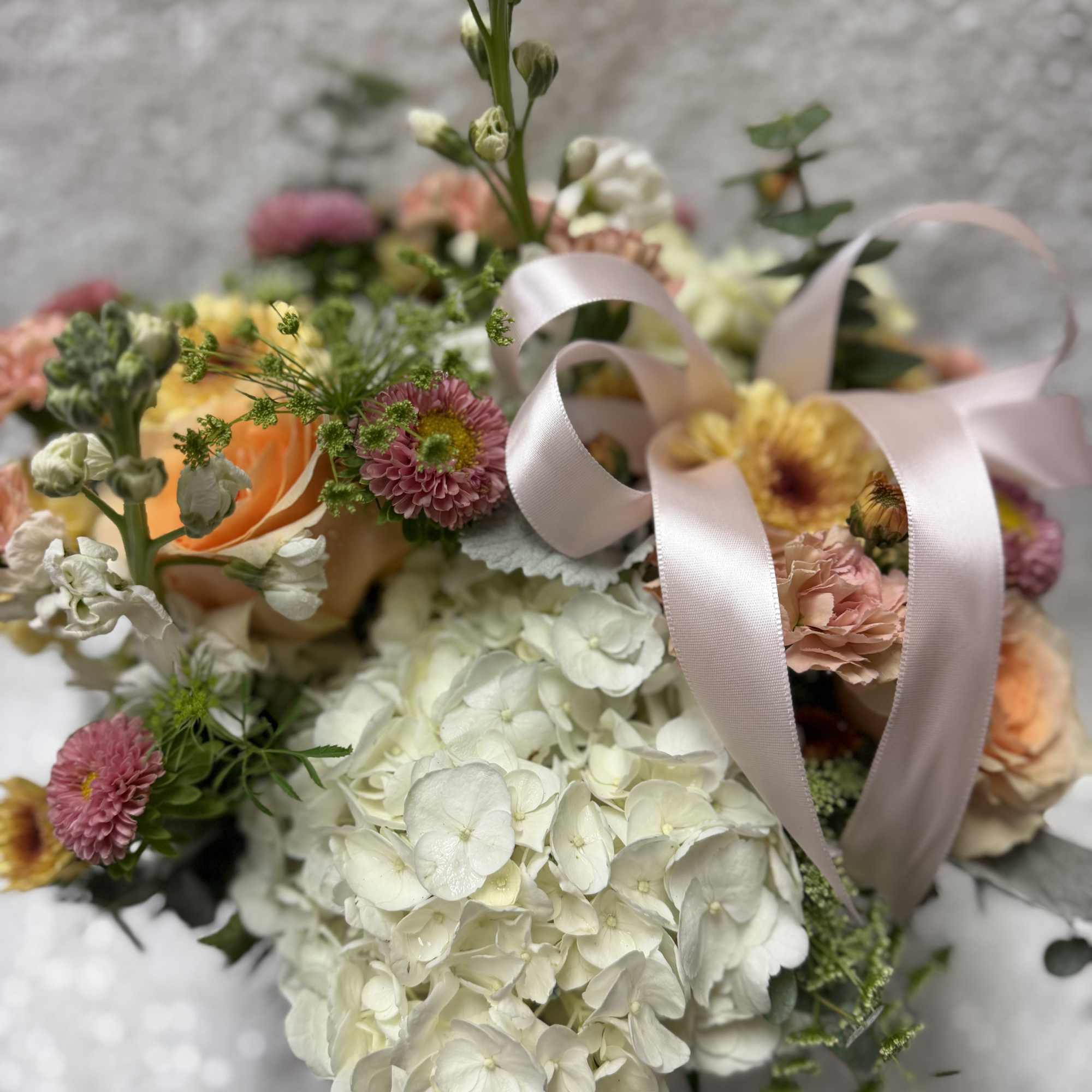 Mixed bouquet with white hydrangeas, peach roses, and pink flowers tied with a pale ribbon