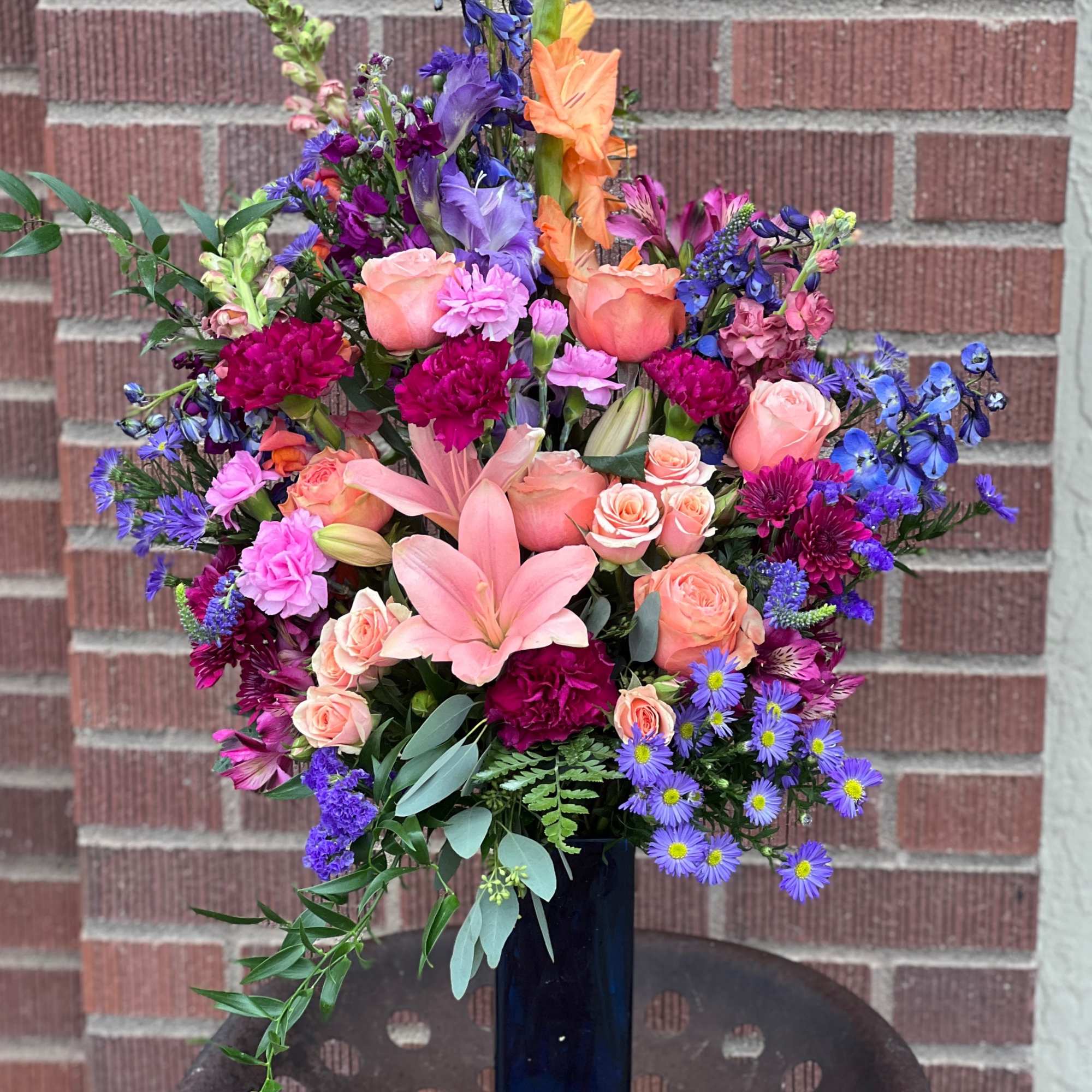 Tall mixed bouquet in a blue vase with pink, orange, and purple flowers