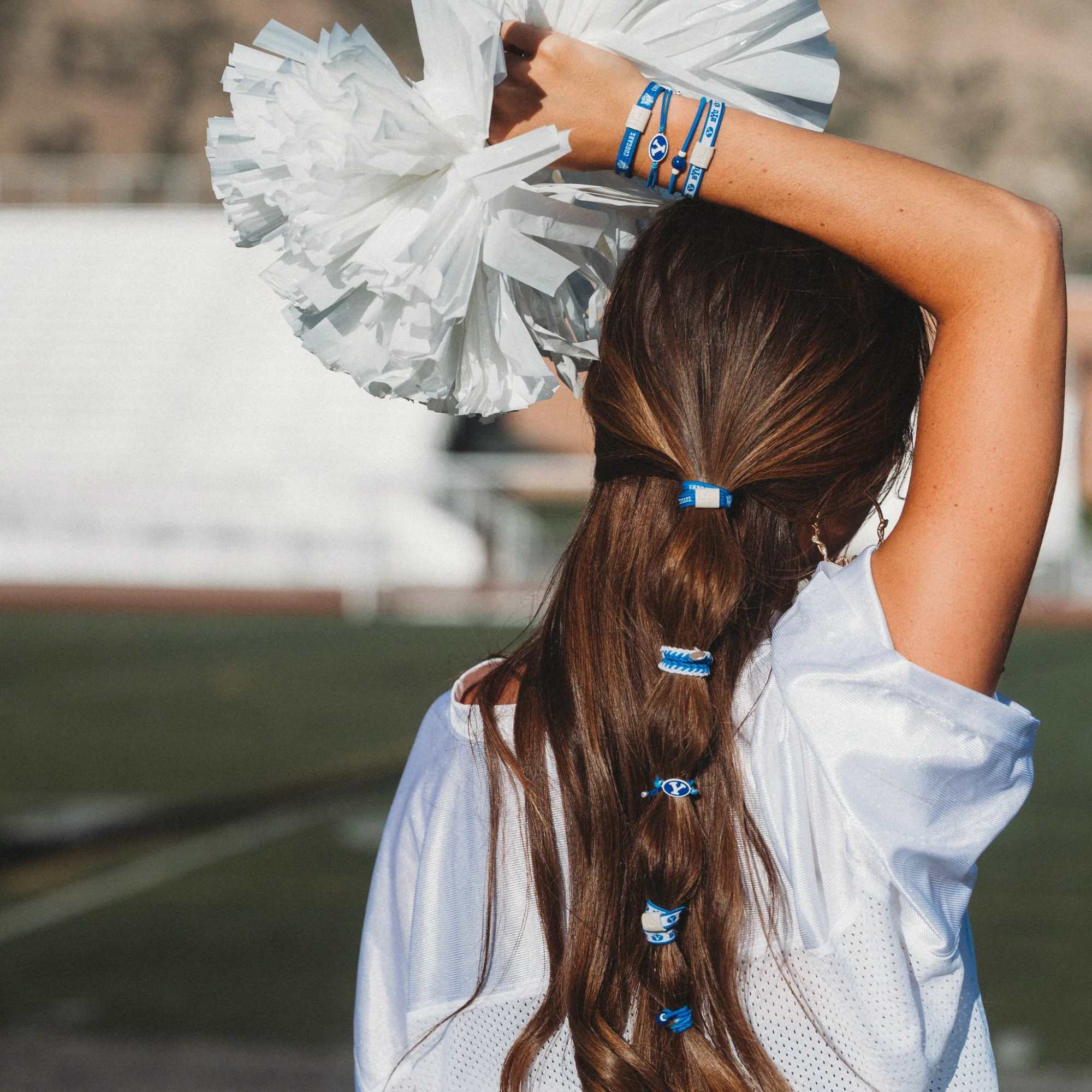 Cheerleader seen from behind holding white pom-poms